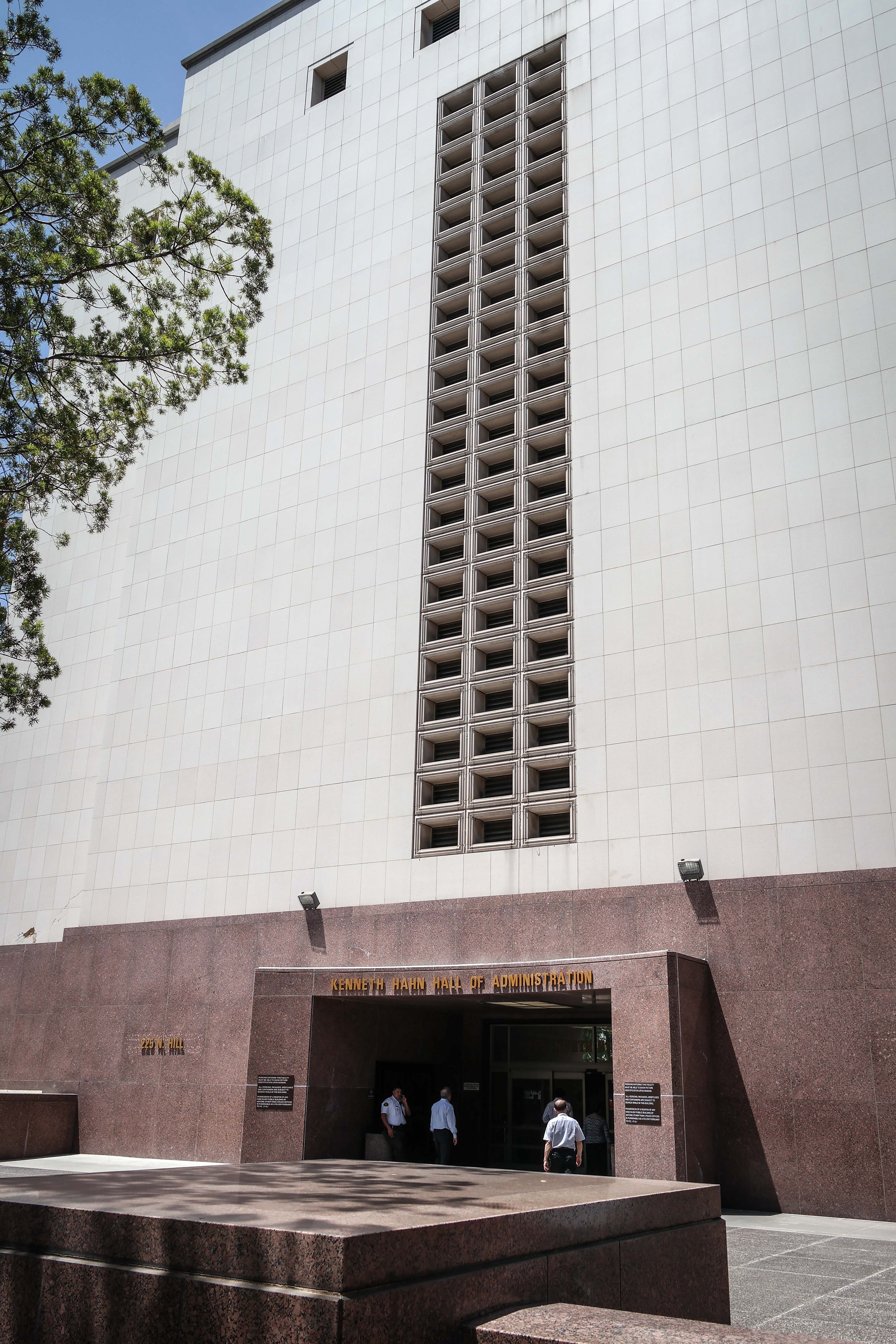 Tall modernist government building with a vertical window grid and people entering at street level.