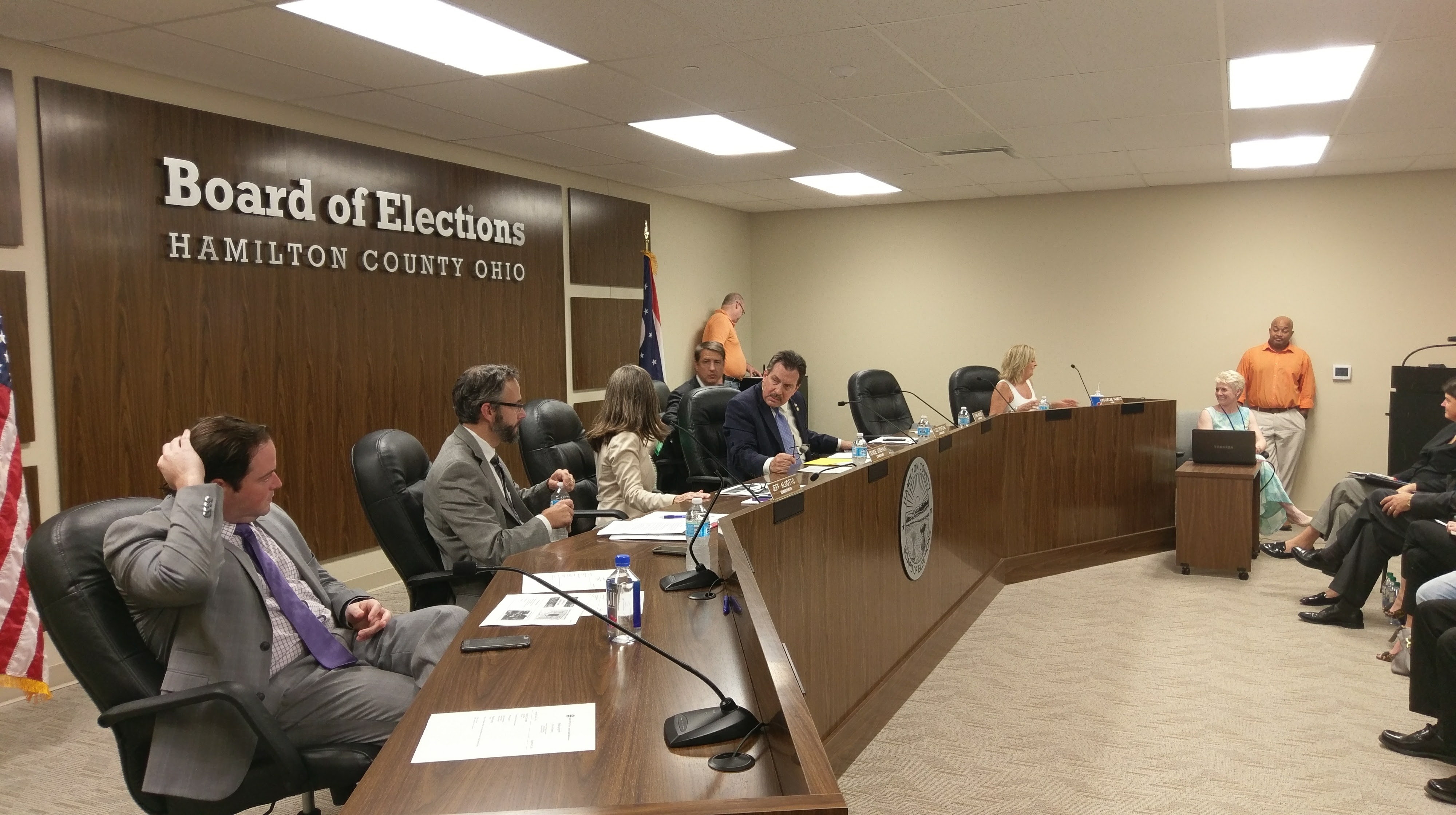 Officials seated at a dais inside a government meeting room with a Board of Elections sign on the wall.