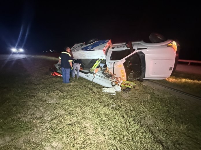 Overturned white commercial truck lying on its side at night with debris scattered around it.