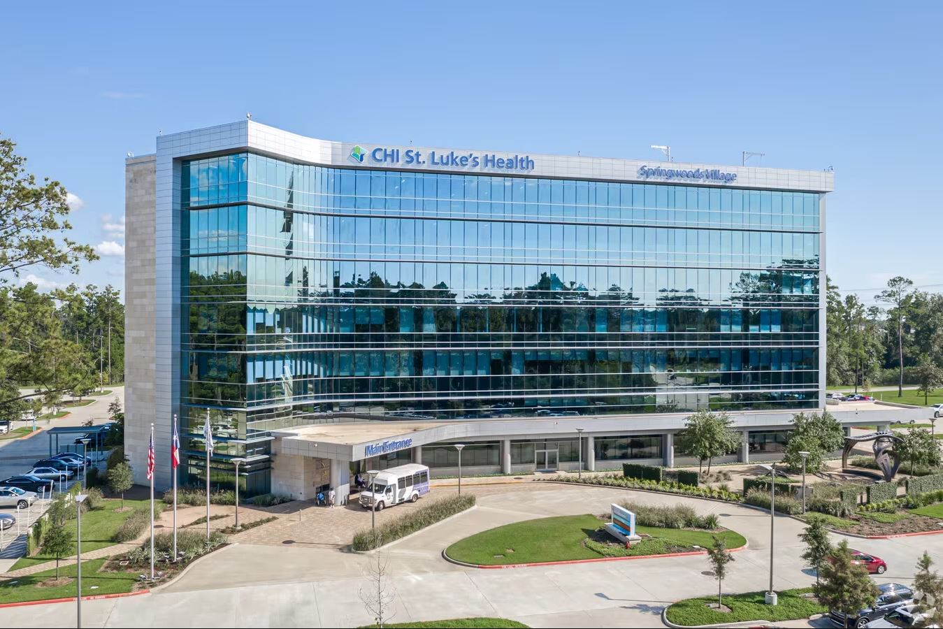 Exterior of CHI St. Luke’s Health Springwoods Village, a modern multi-story glass building with landscaped grounds, parking areas and a circular driveway.