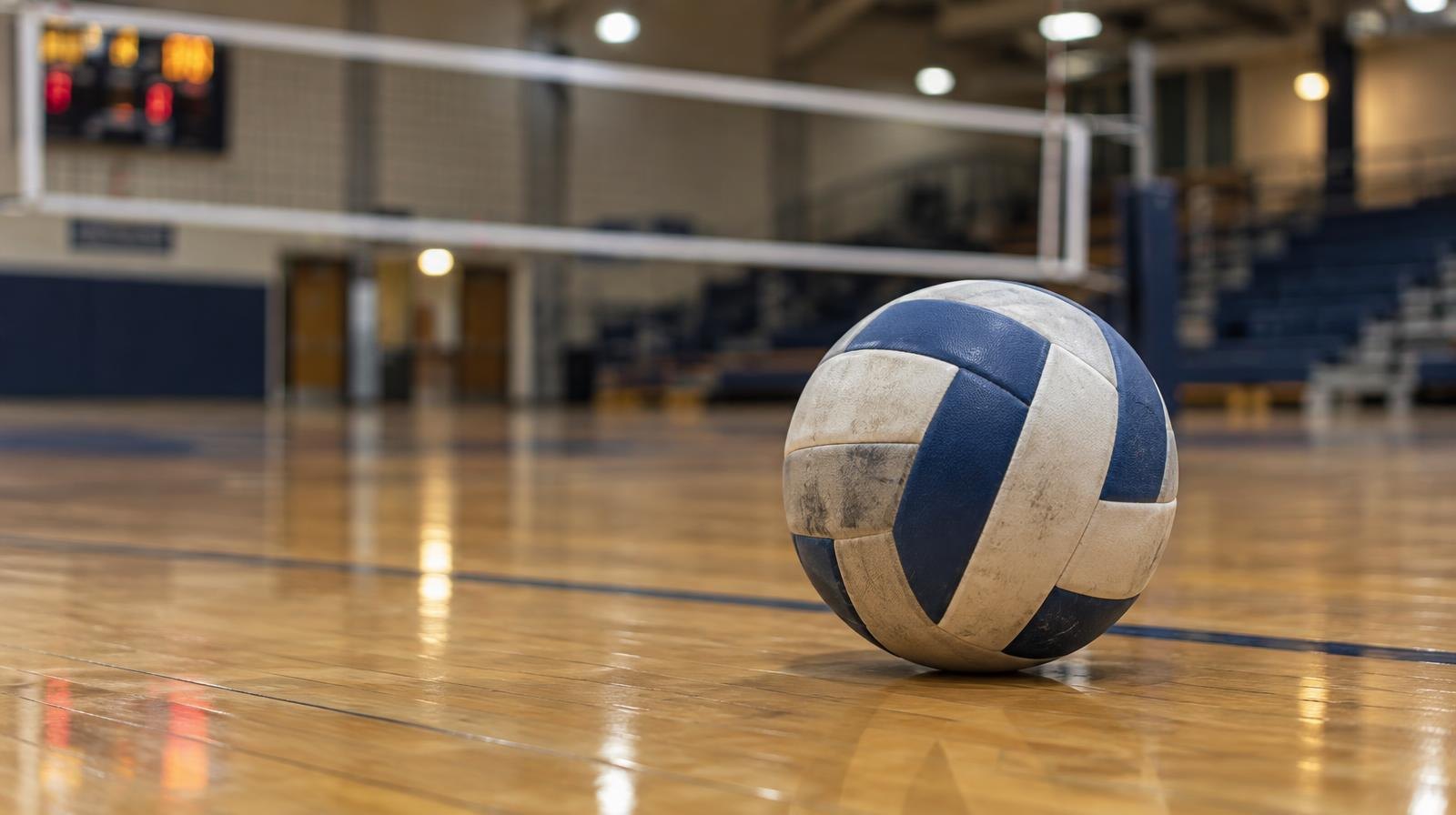 A volleyball resting on a hardwood gym floor near the net.