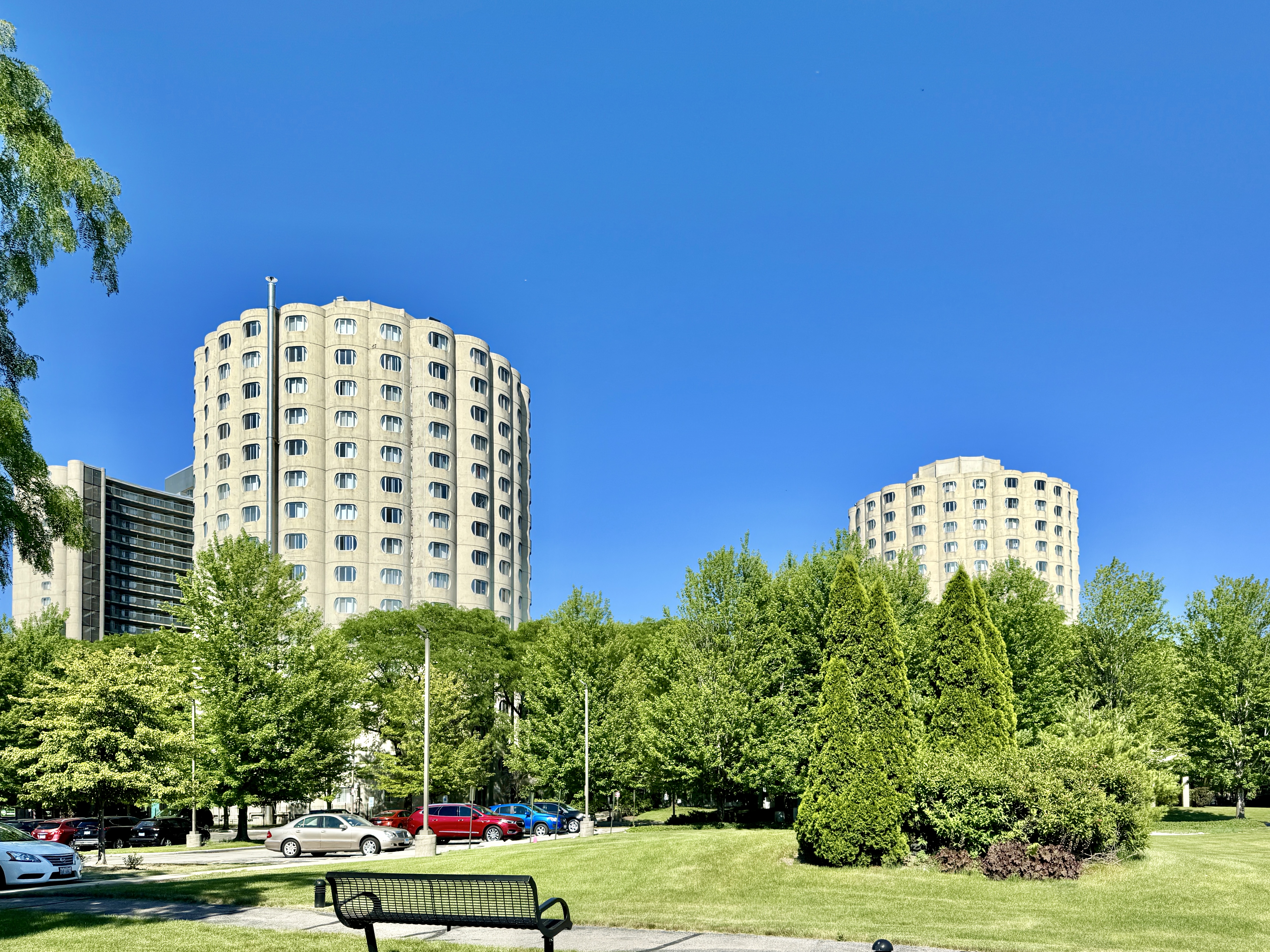 Two cylindrical high-rise apartment towers surrounded by trees and landscaped grounds.