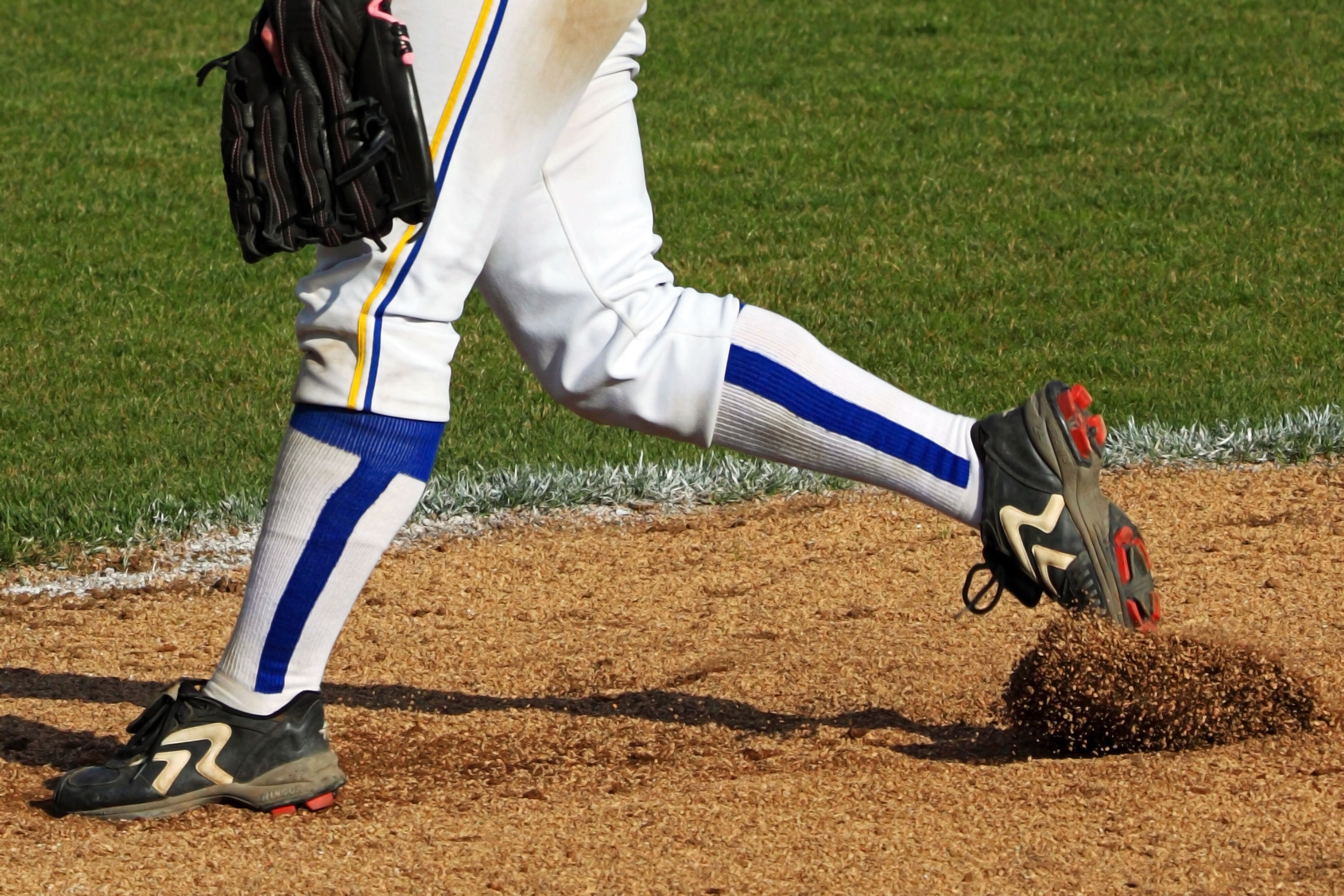 Lower body of a softball pitcher in uniform standing on a dirt pitching mound.