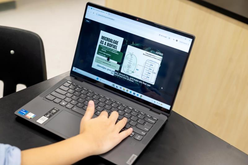 A hand rests on a laptop keyboard showing a presentation slide titled Microalgae as a Biofuel.