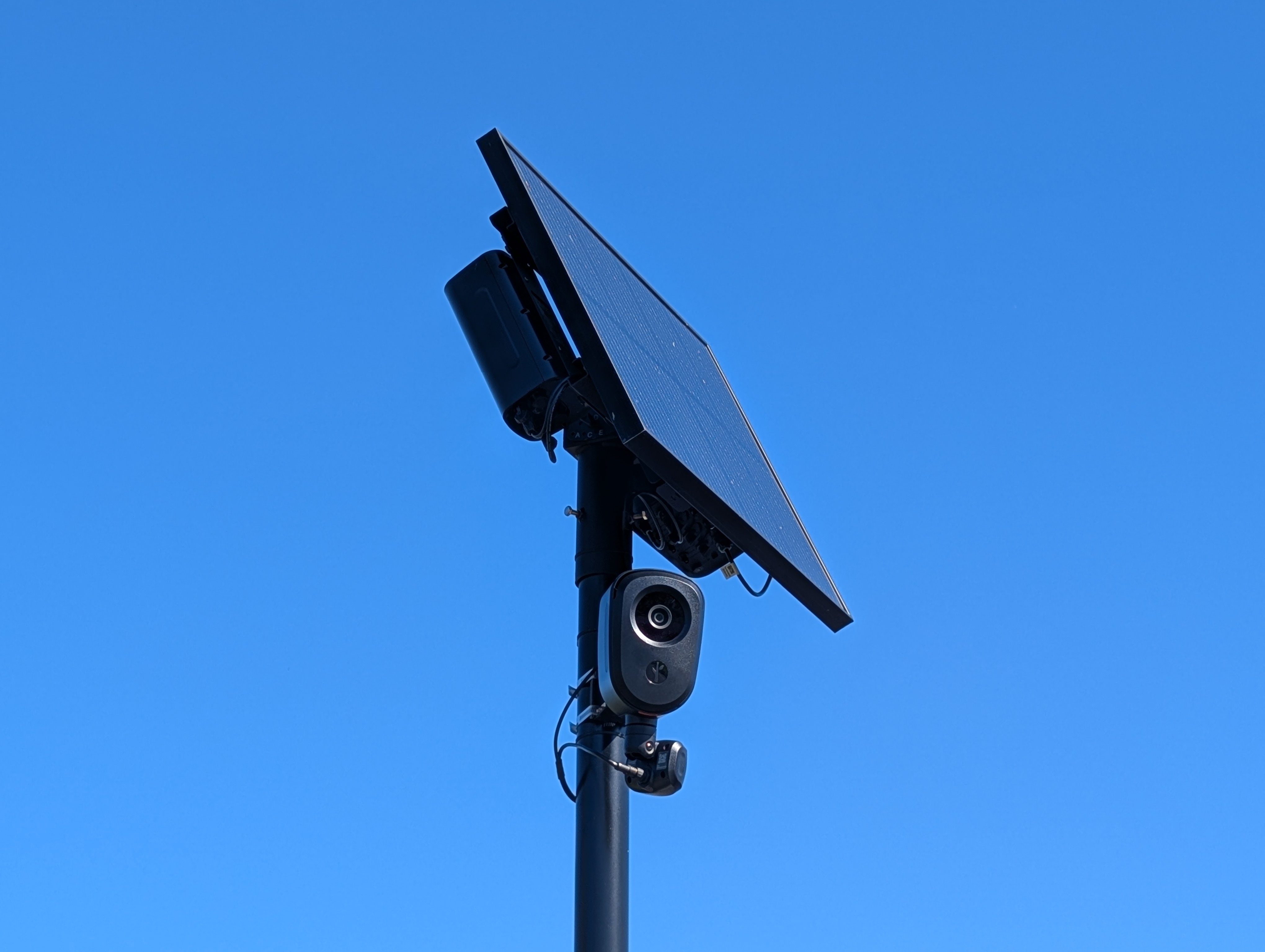 Close-up of a solar-powered license plate reader camera mounted on a metal pole against blue sky.