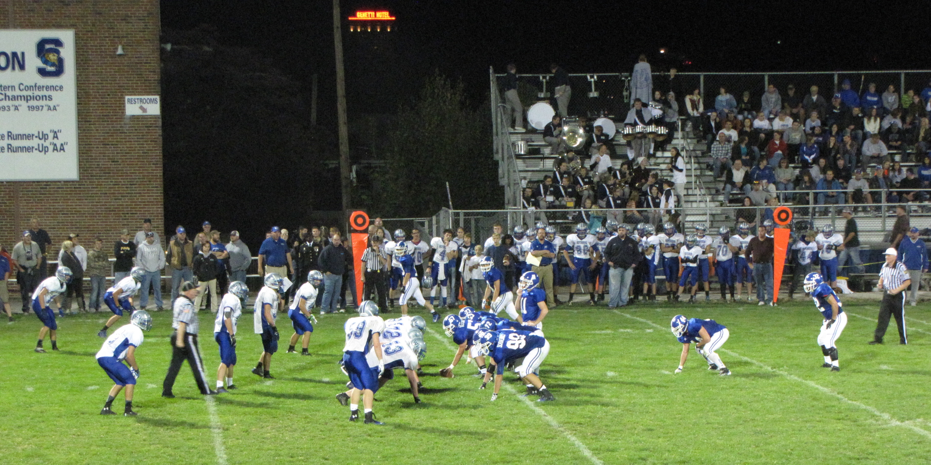 Football players in blue and white uniforms compete on a lit field at night.