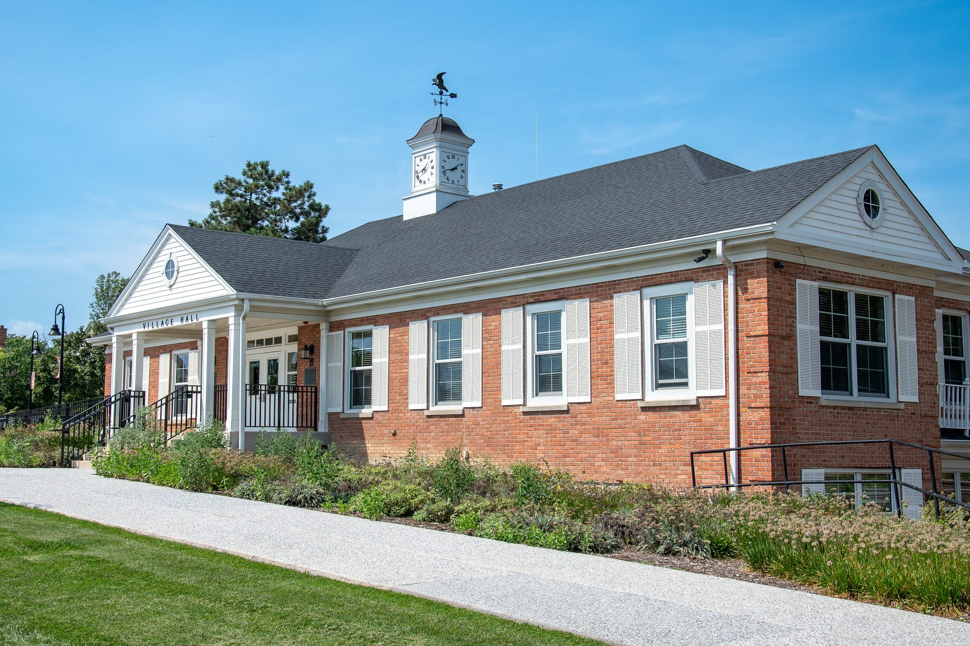 Single-story red-brick village hall with clock cupola and landscaped walkway.