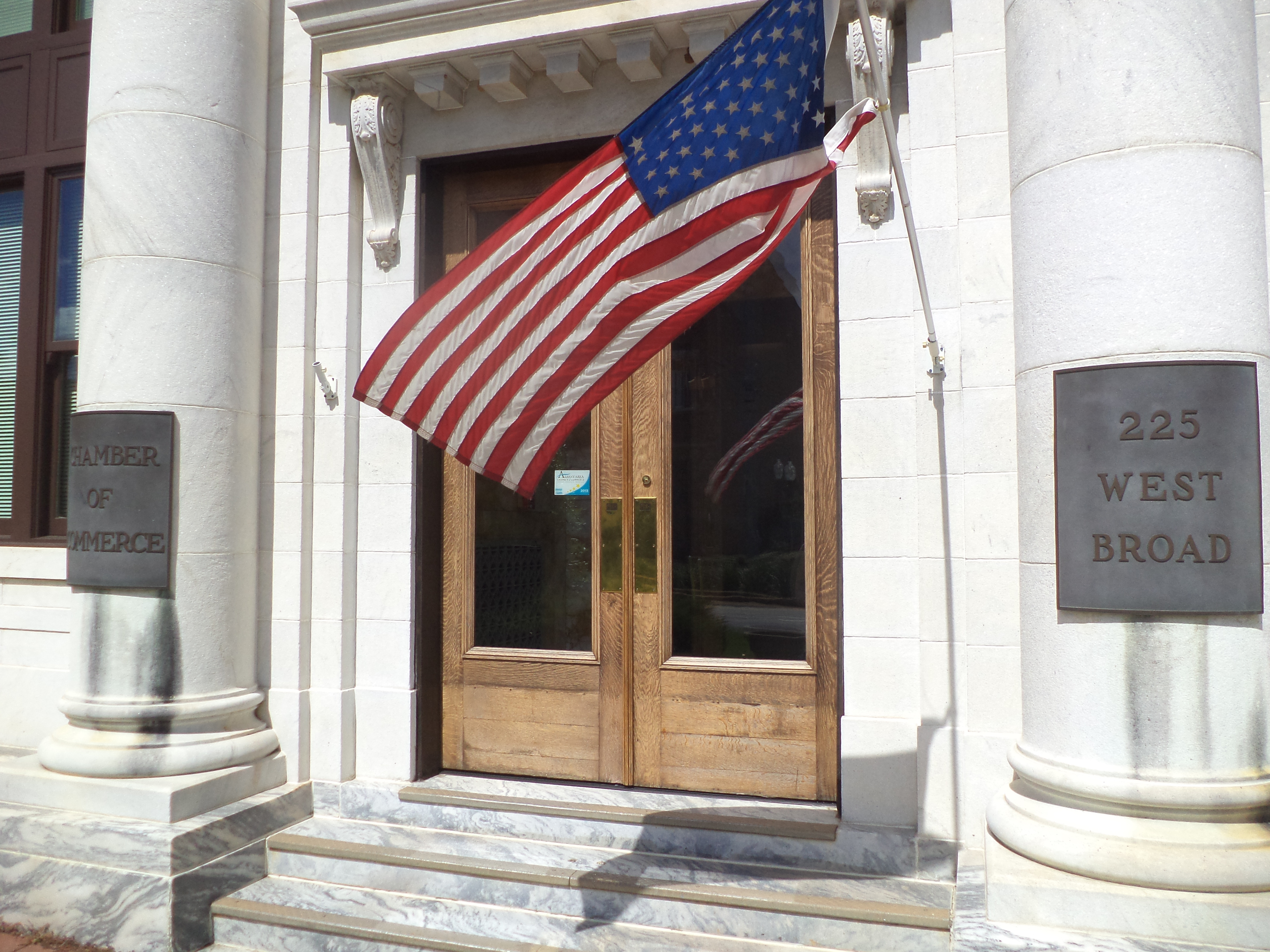 Stone-columned chamber of commerce building entrance with wooden doors and a Chamber of Commerce plaque.