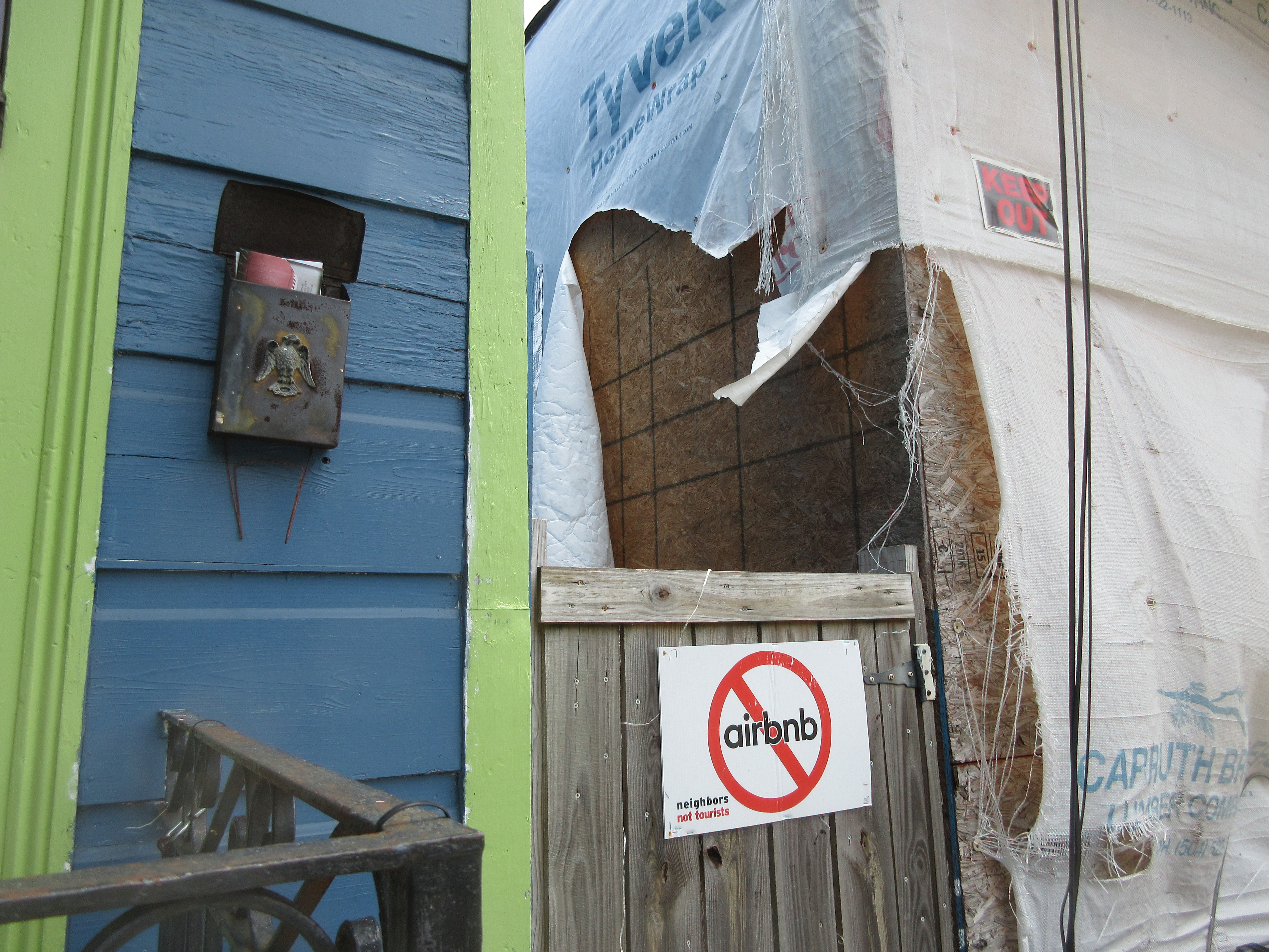Red no-symbol over the Airbnb logo on a wooden gate, with text reading 'neighbors not hotels.'