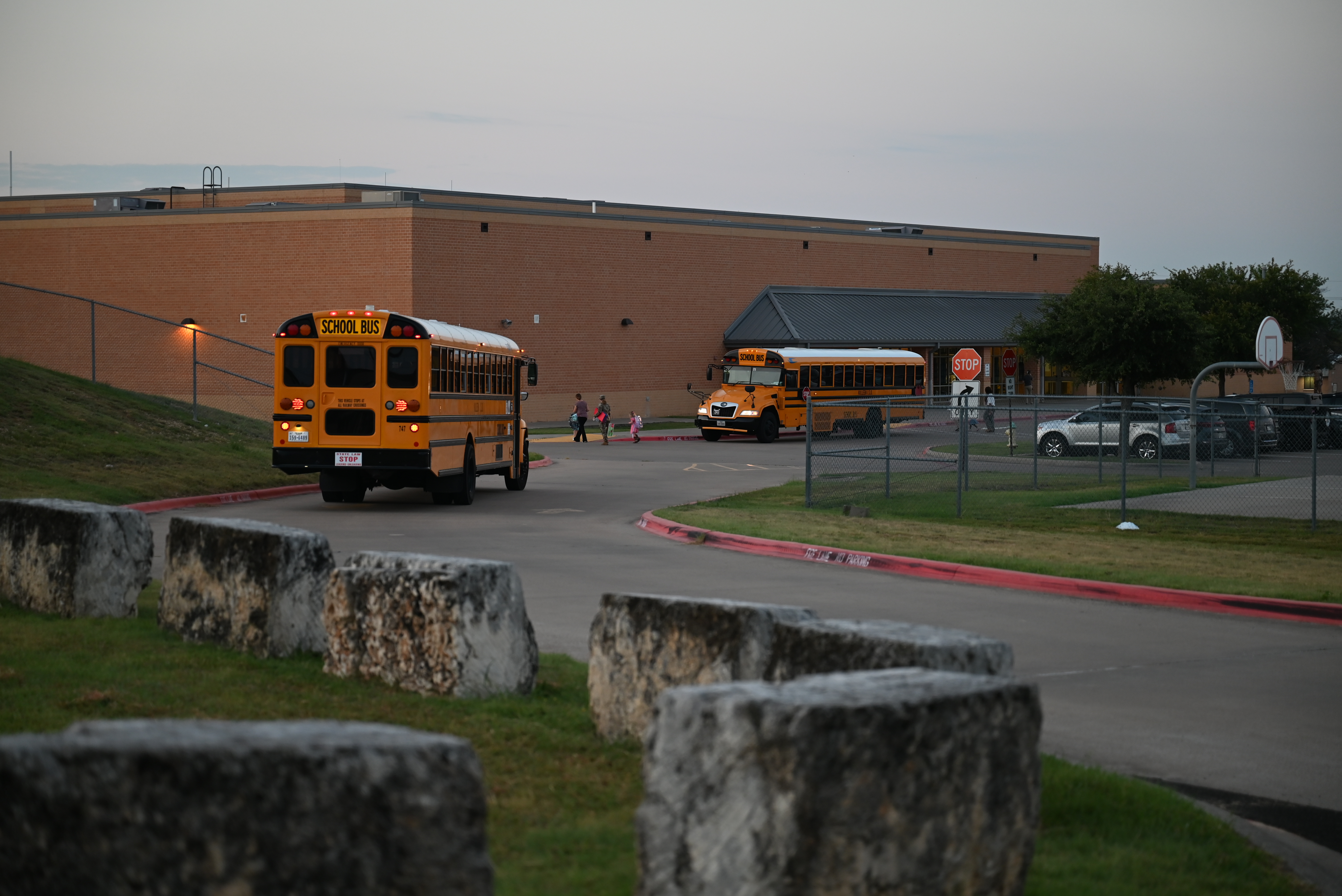 Two yellow school buses parked in front of a large brick school building at dusk.