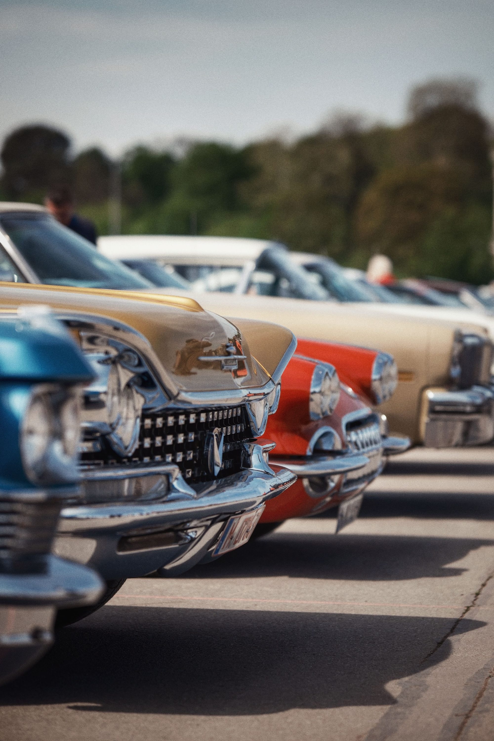 Colorful vintage cars lined up in perfect alignment at an outdoor car show under a clear sky.