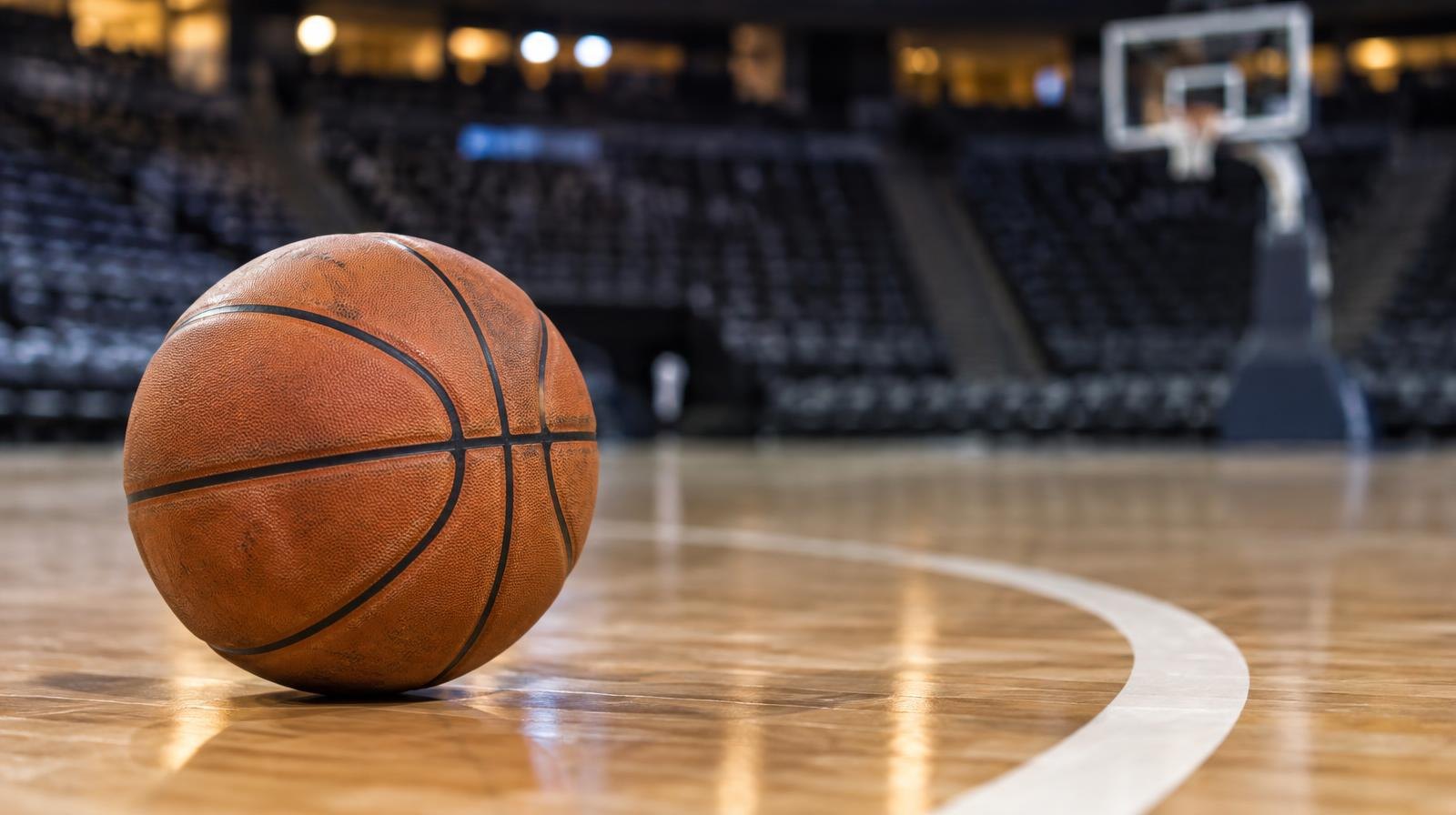A basketball resting on a hardwood court floor near a painted arc line.