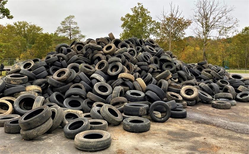 Large pile of hundreds of used car and truck tires stacked outdoors on pavement.