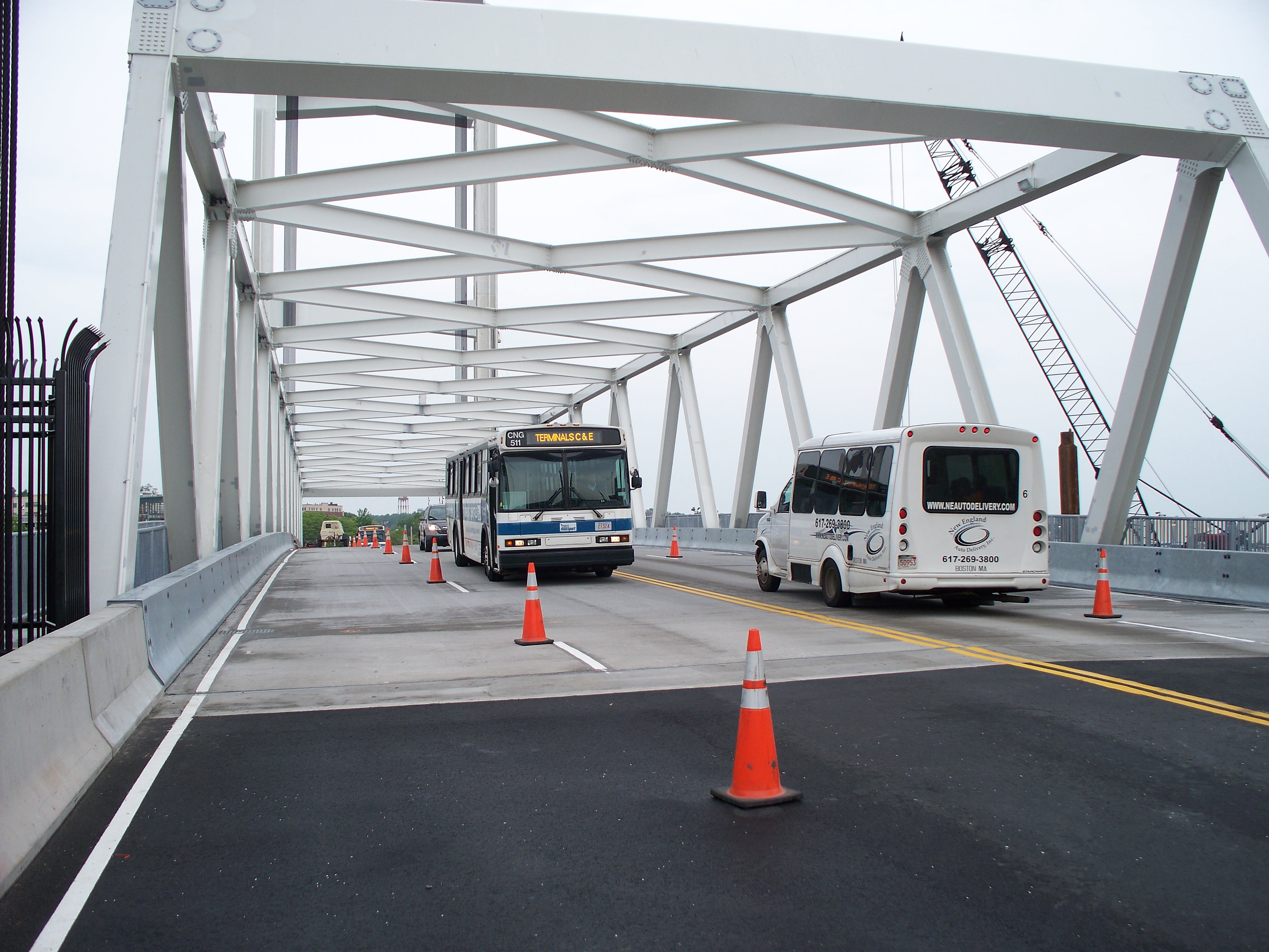 A bridge with orange traffic cones narrowing lanes, a bus and van crossing.