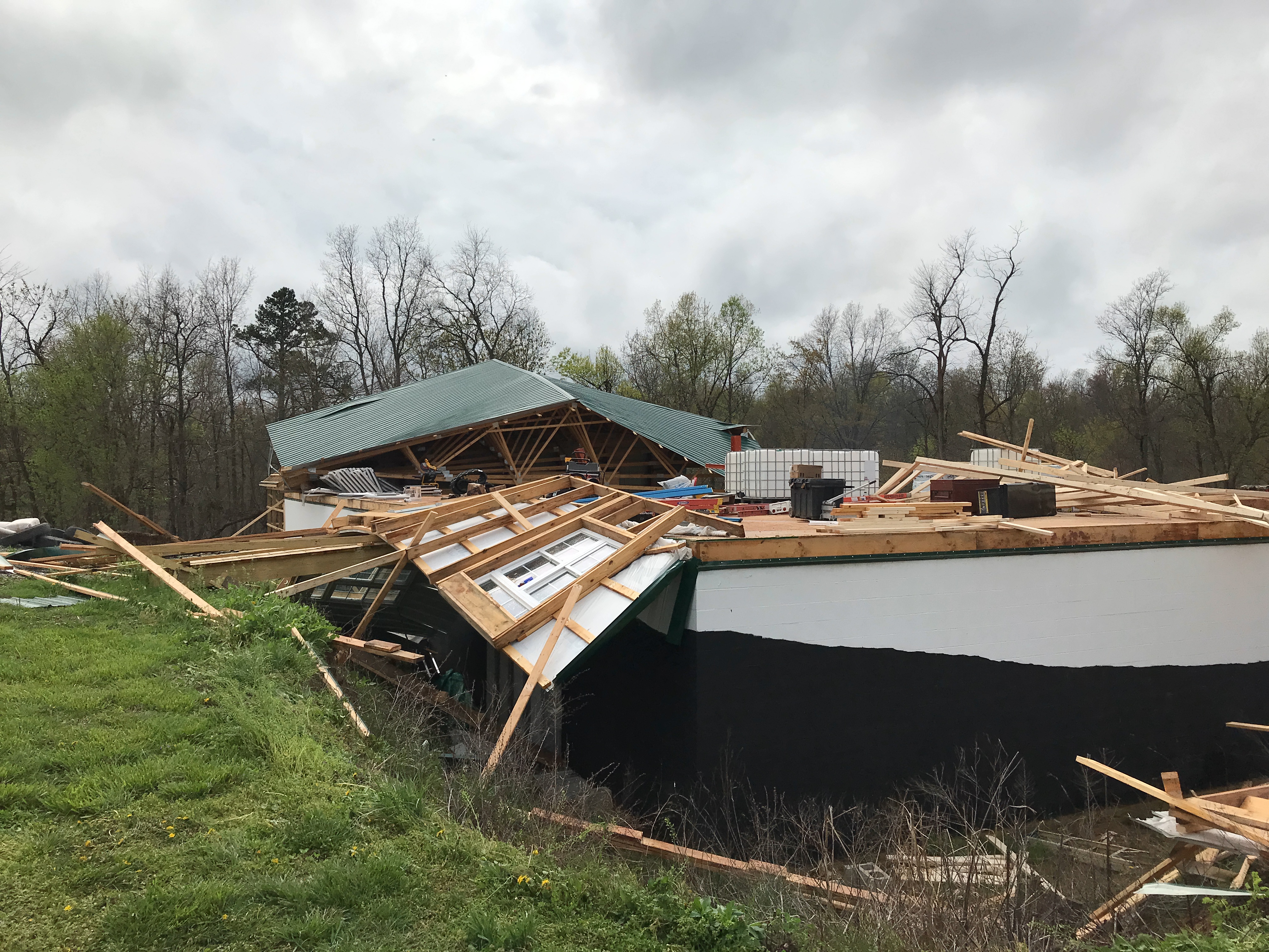 Collapsed green metal roof and scattered lumber debris from a destroyed rural building.