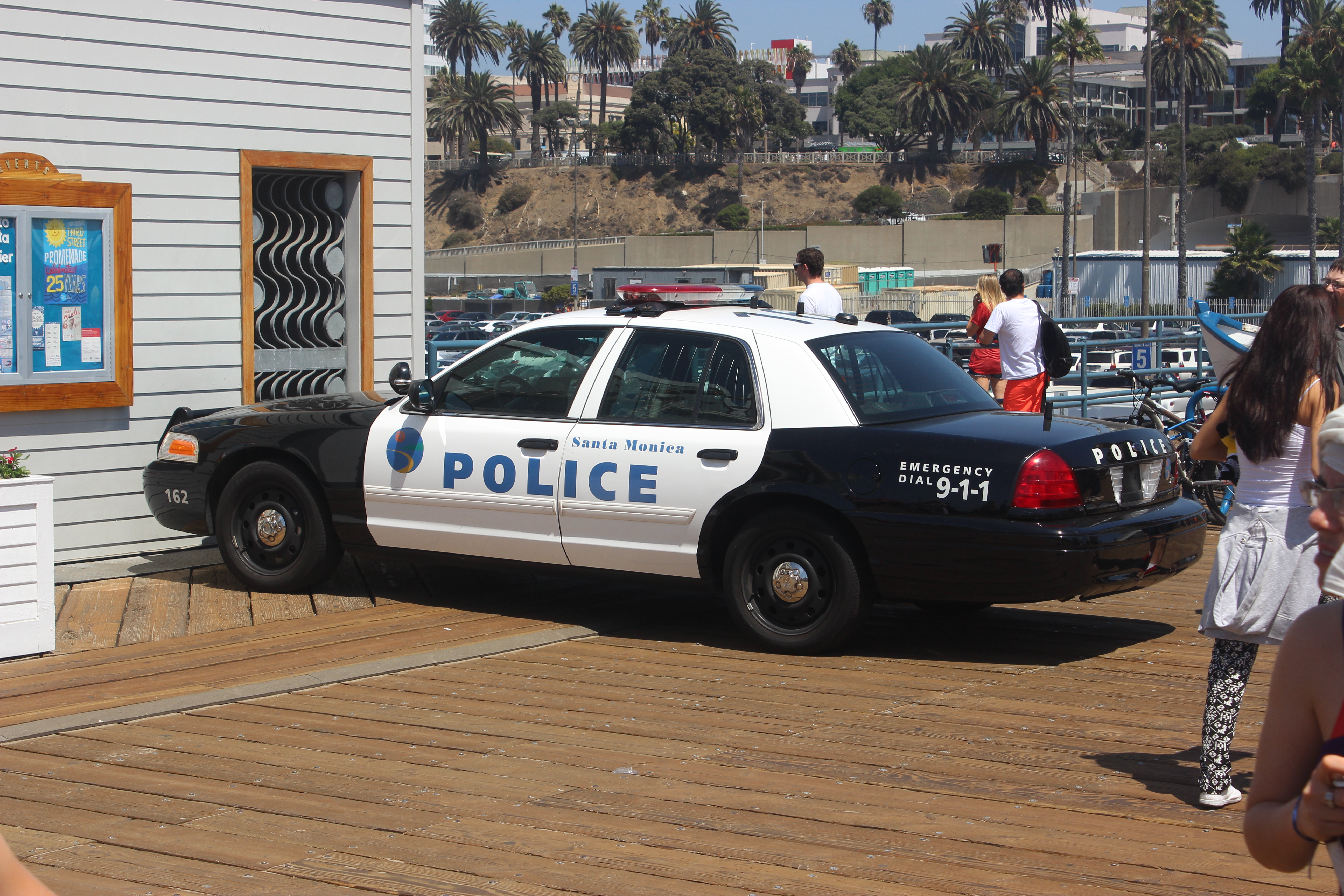 Black and white Santa Monica Police patrol car parked on the pier with palm trees behind it.