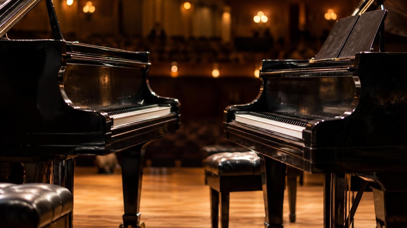 Two black grand pianos facing each other on a spotlit concert stage.