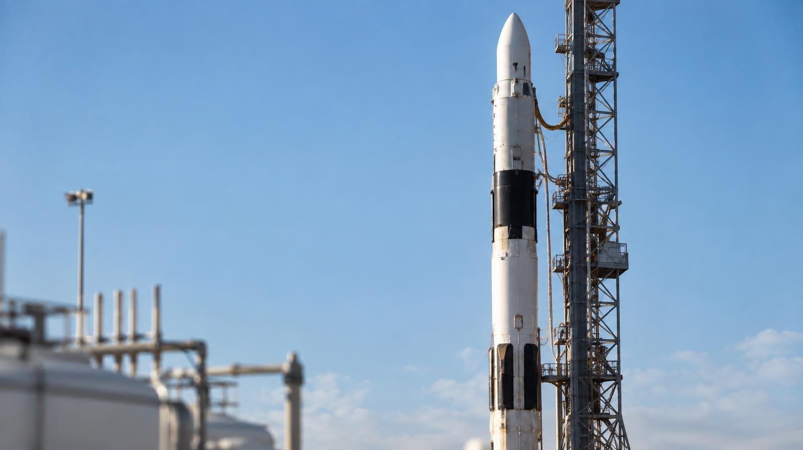 A rocket standing upright on a launch pad against a clear blue sky.