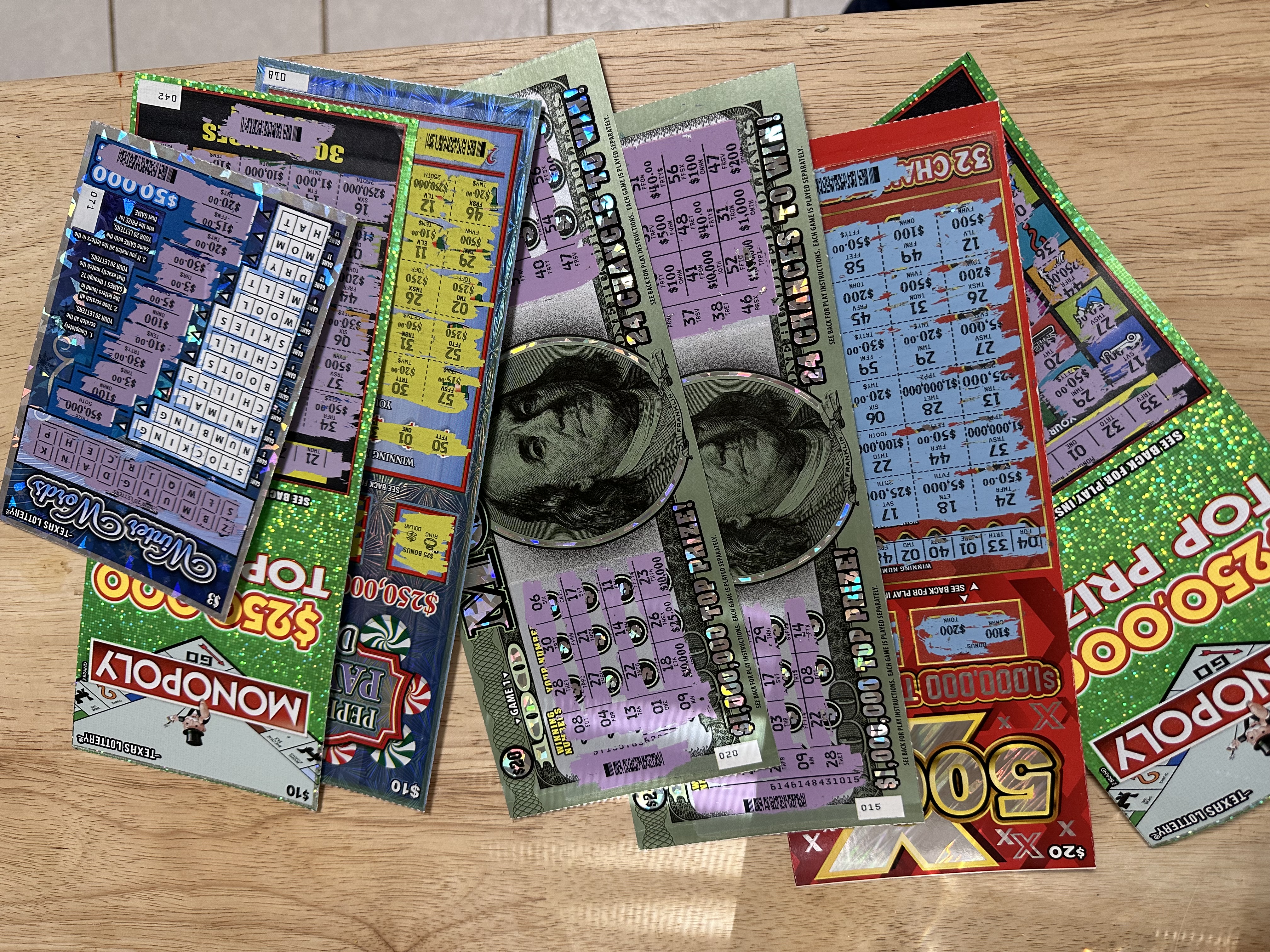Several scratch-off lottery tickets fanned out on a wooden table with a $100 bill.