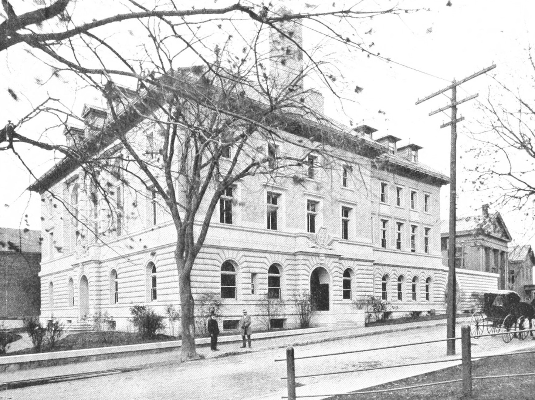 Historic black-and-white photo of a large stone police station building with bare trees in front.