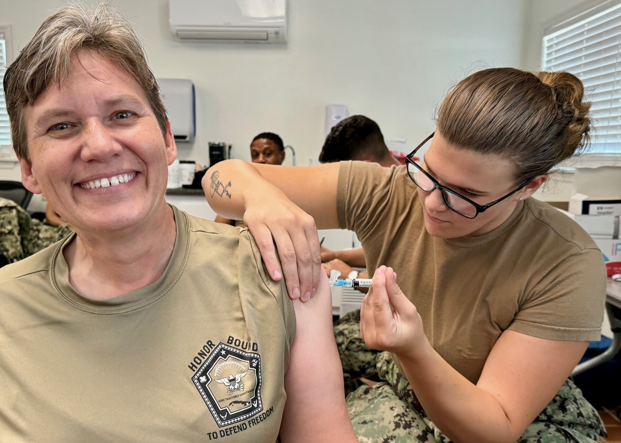 A woman smiles while receiving a flu shot injection in her upper arm.