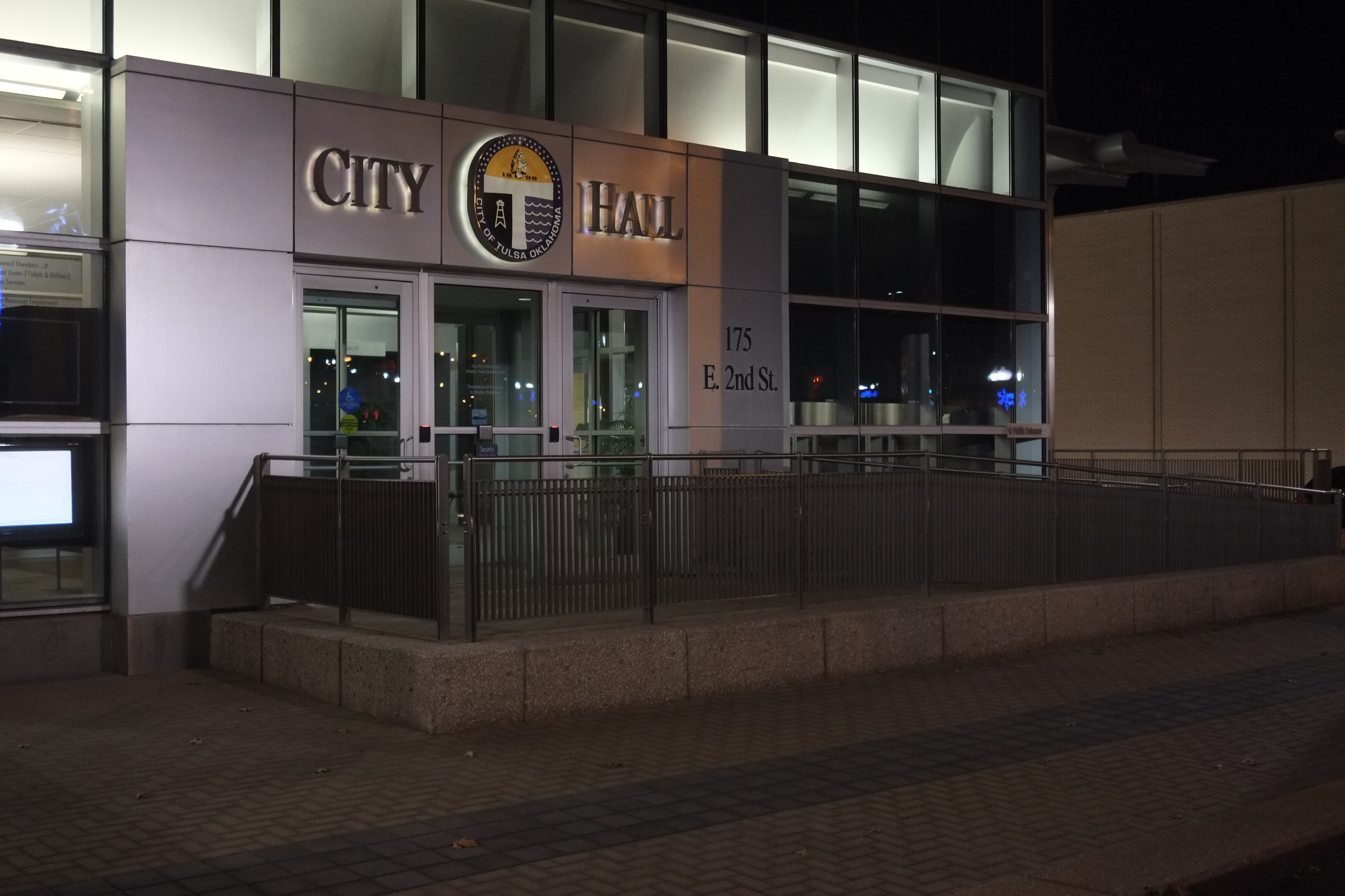Tulsa City Hall exterior at night, with lit signage and glass entrance doors.