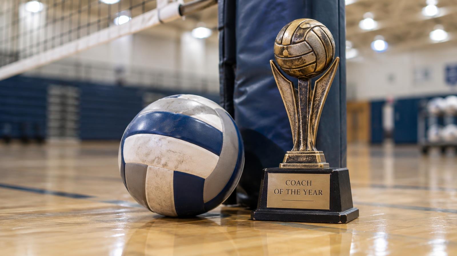 A volleyball on a gym floor beside a net post and a trophy.