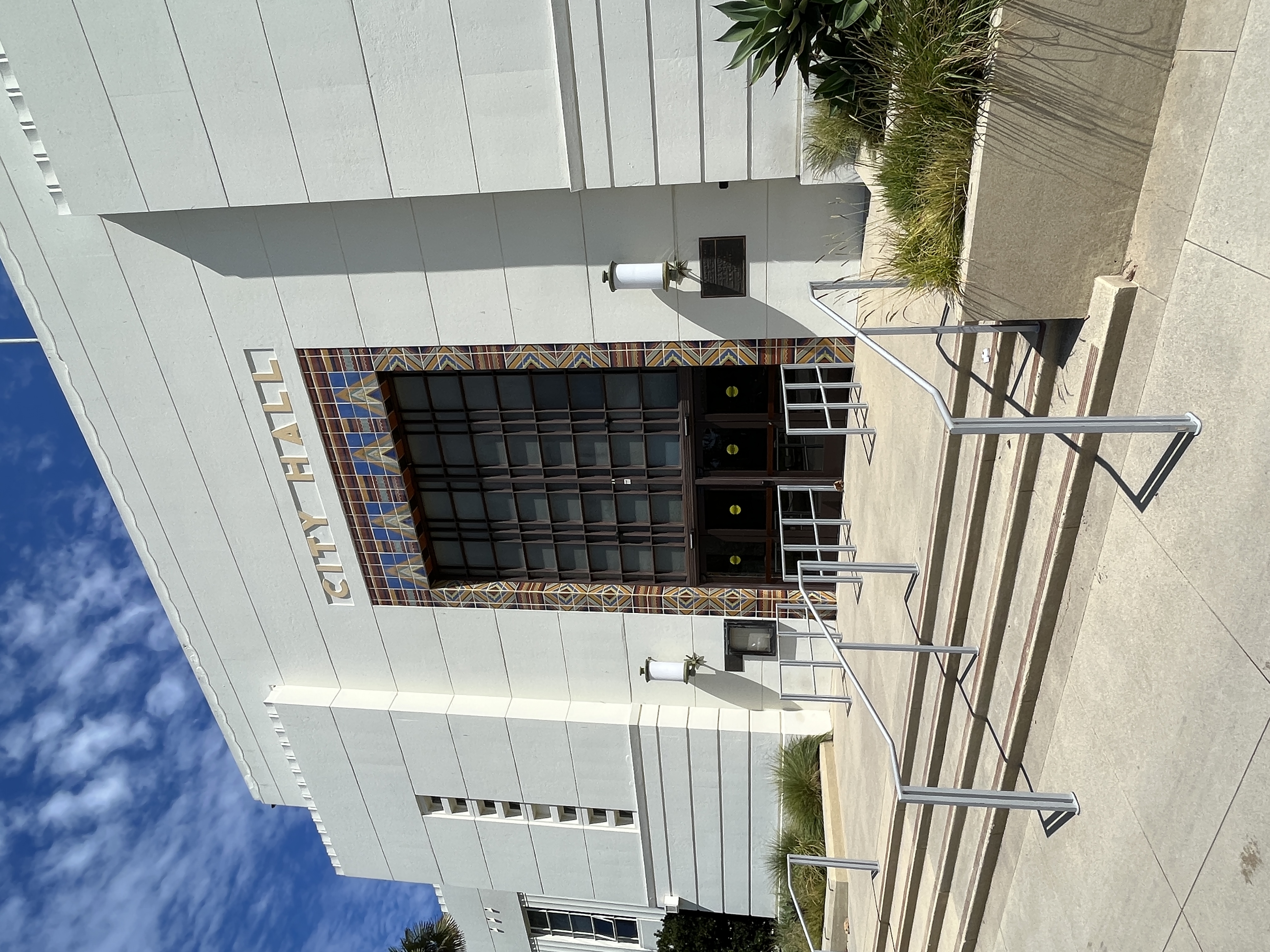 Art Deco white building entrance with 'CITY HALL' lettering above the doors and metal railings on the steps.
