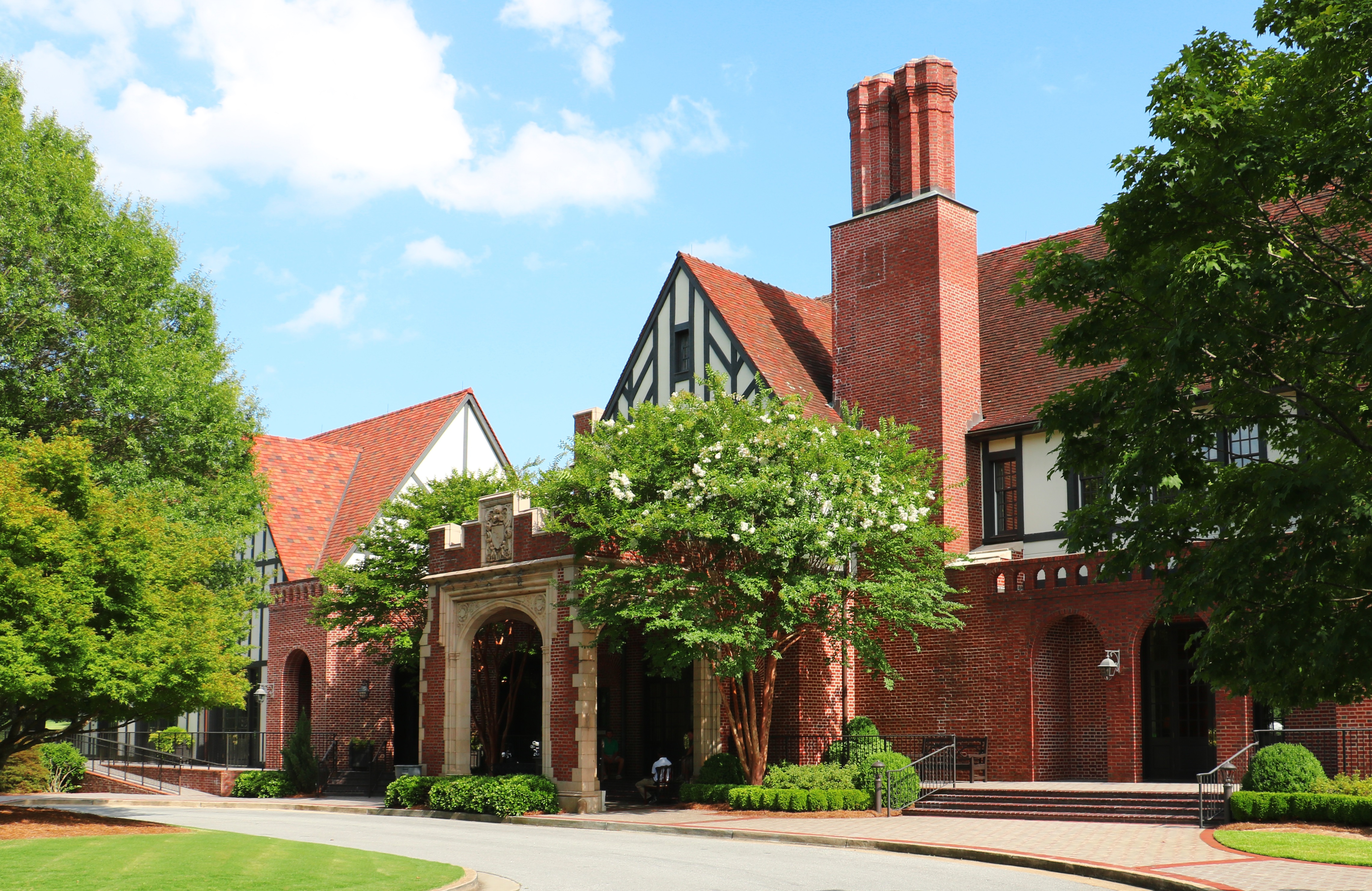 Tudor-style red-brick golf clubhouse with arched entrance and mature trees.