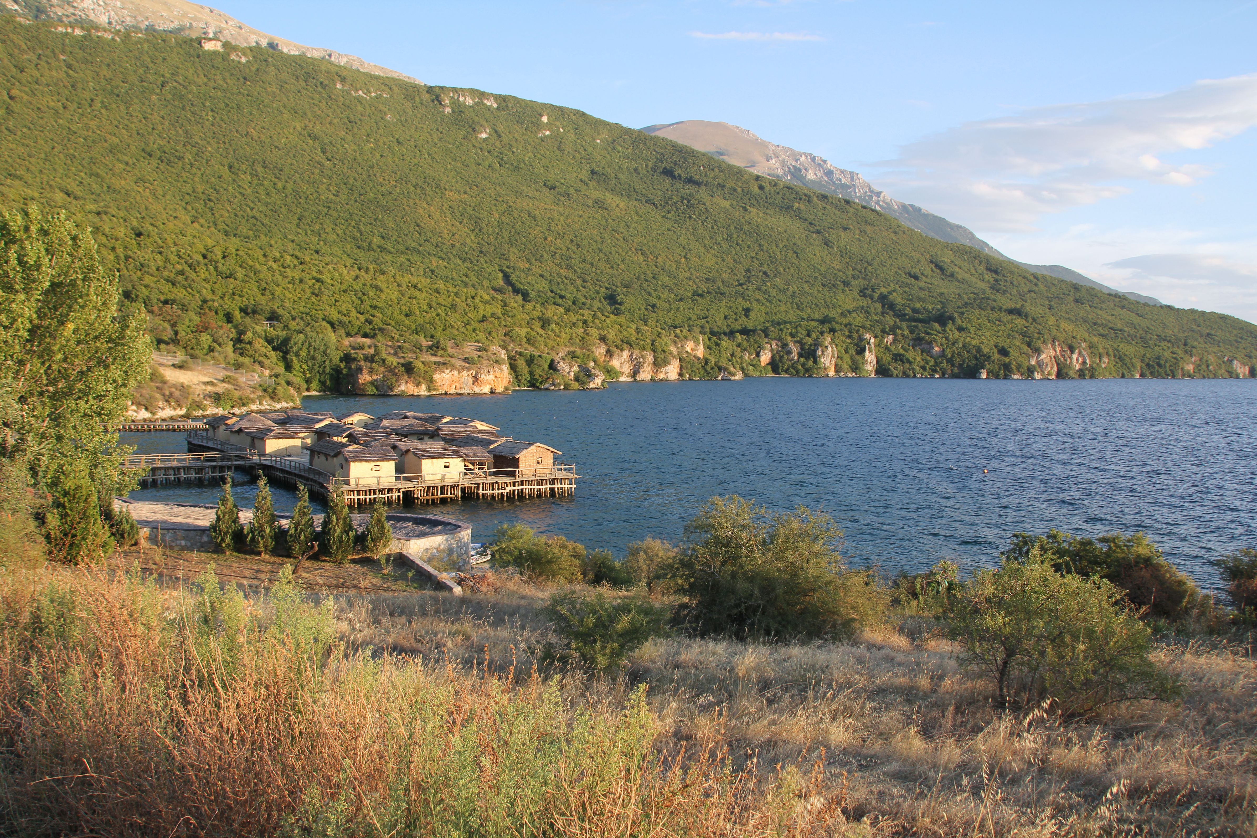 Reconstructed prehistoric stilt houses on a wooden platform over a calm lake.