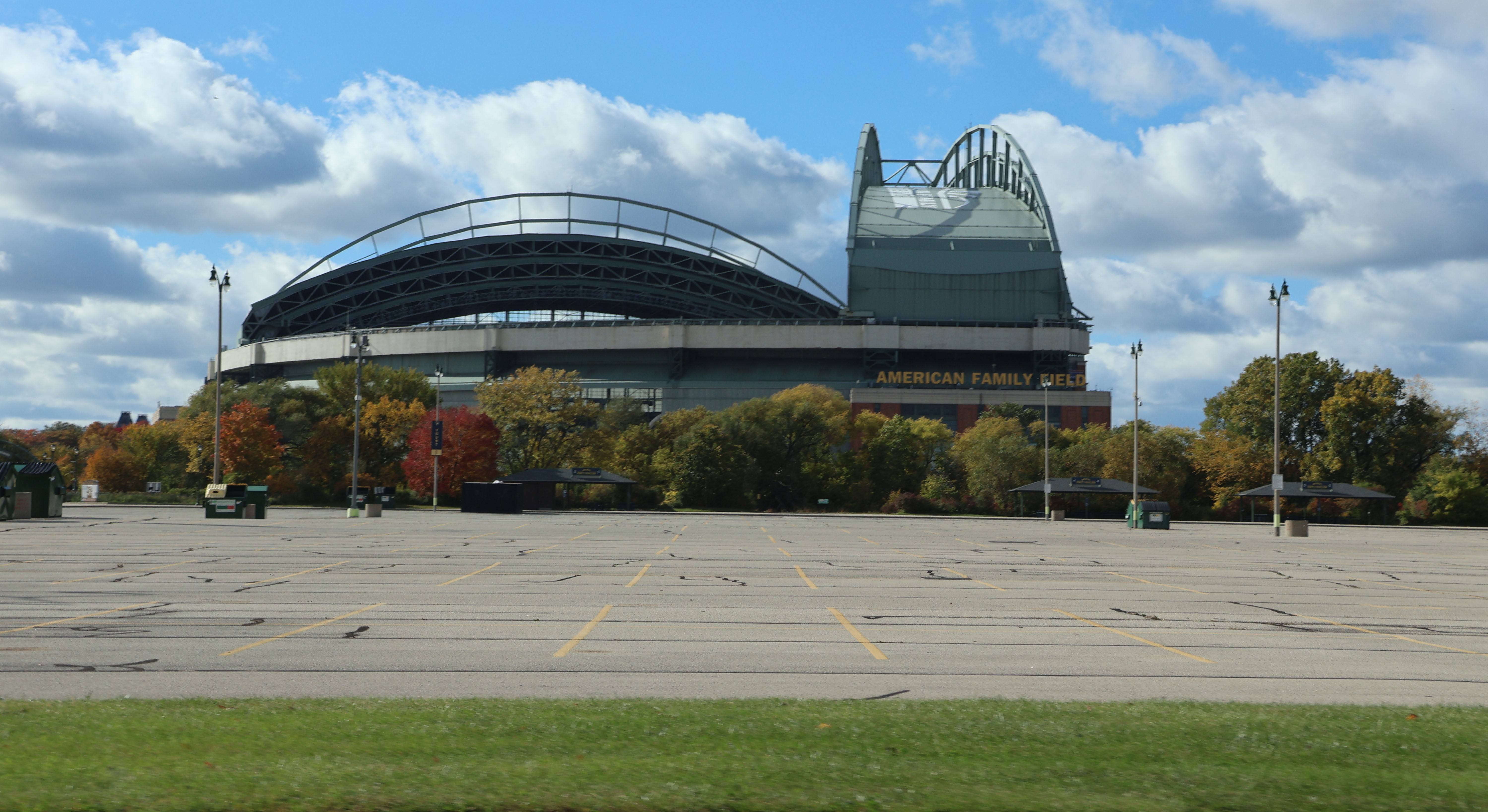 Exterior of a large domed baseball stadium surrounded by autumn trees and an empty parking lot.
