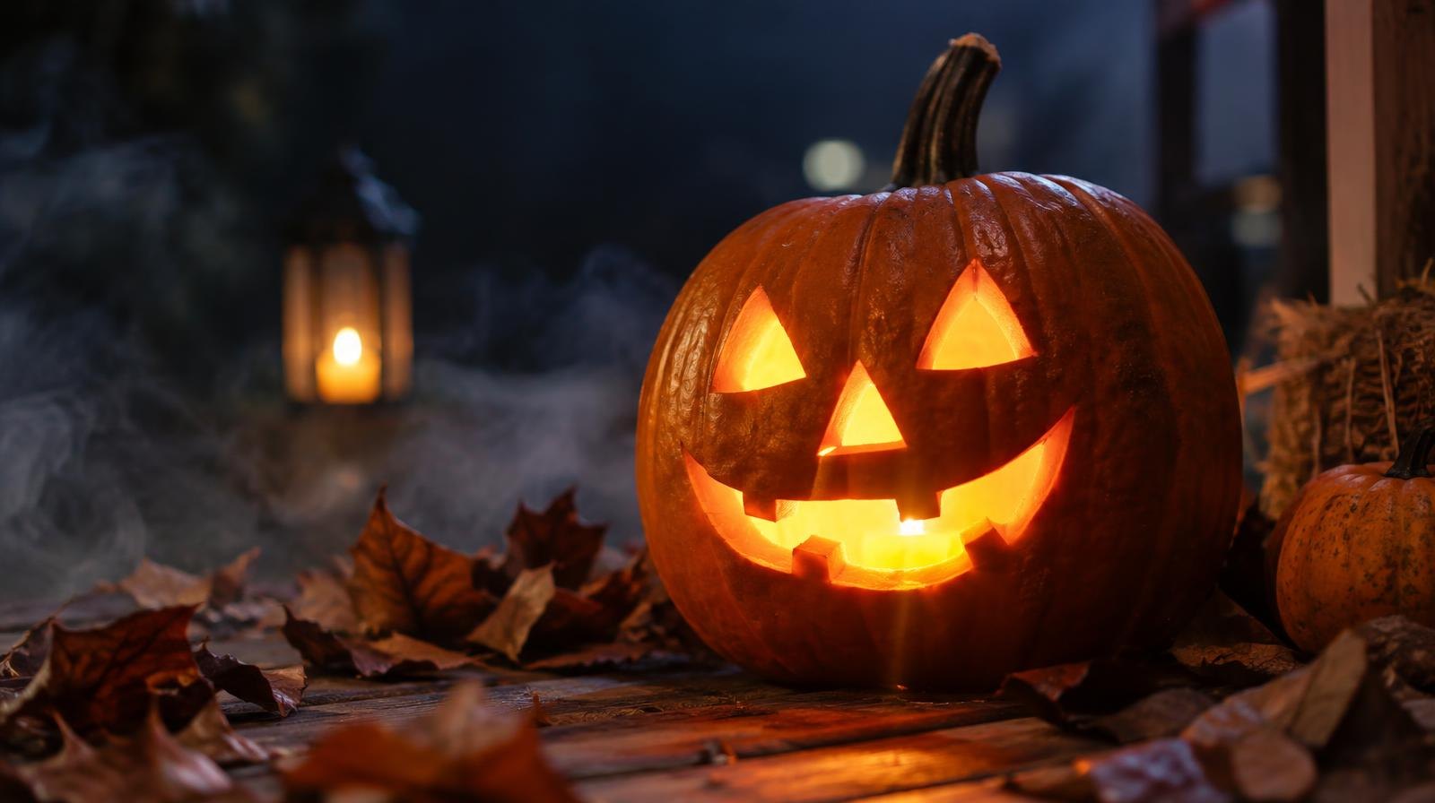 A glowing carved pumpkin surrounded by autumn leaves and wisps of fog at night.
