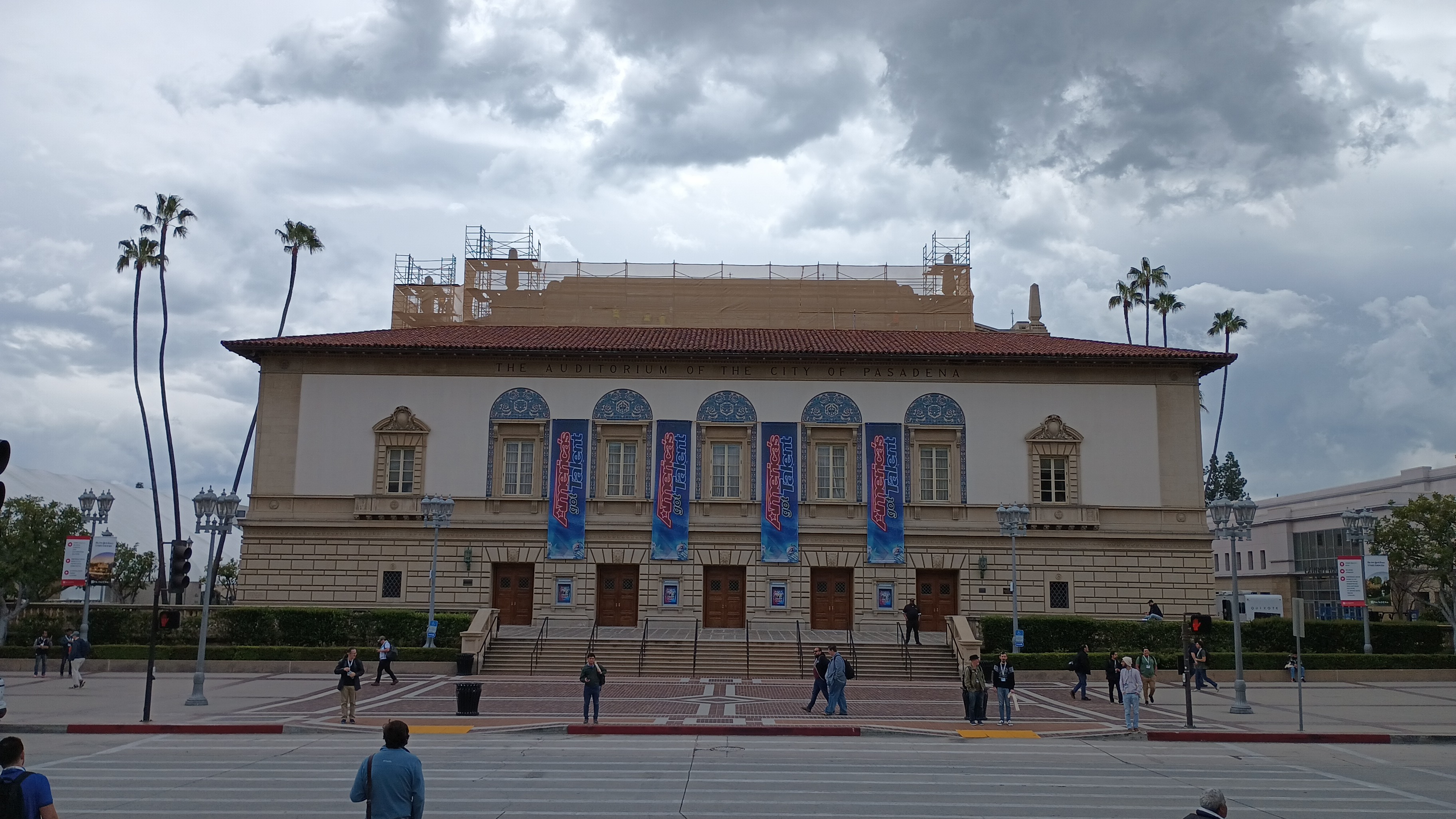 Classical-style civic auditorium facade with blue banners and palm trees out front.