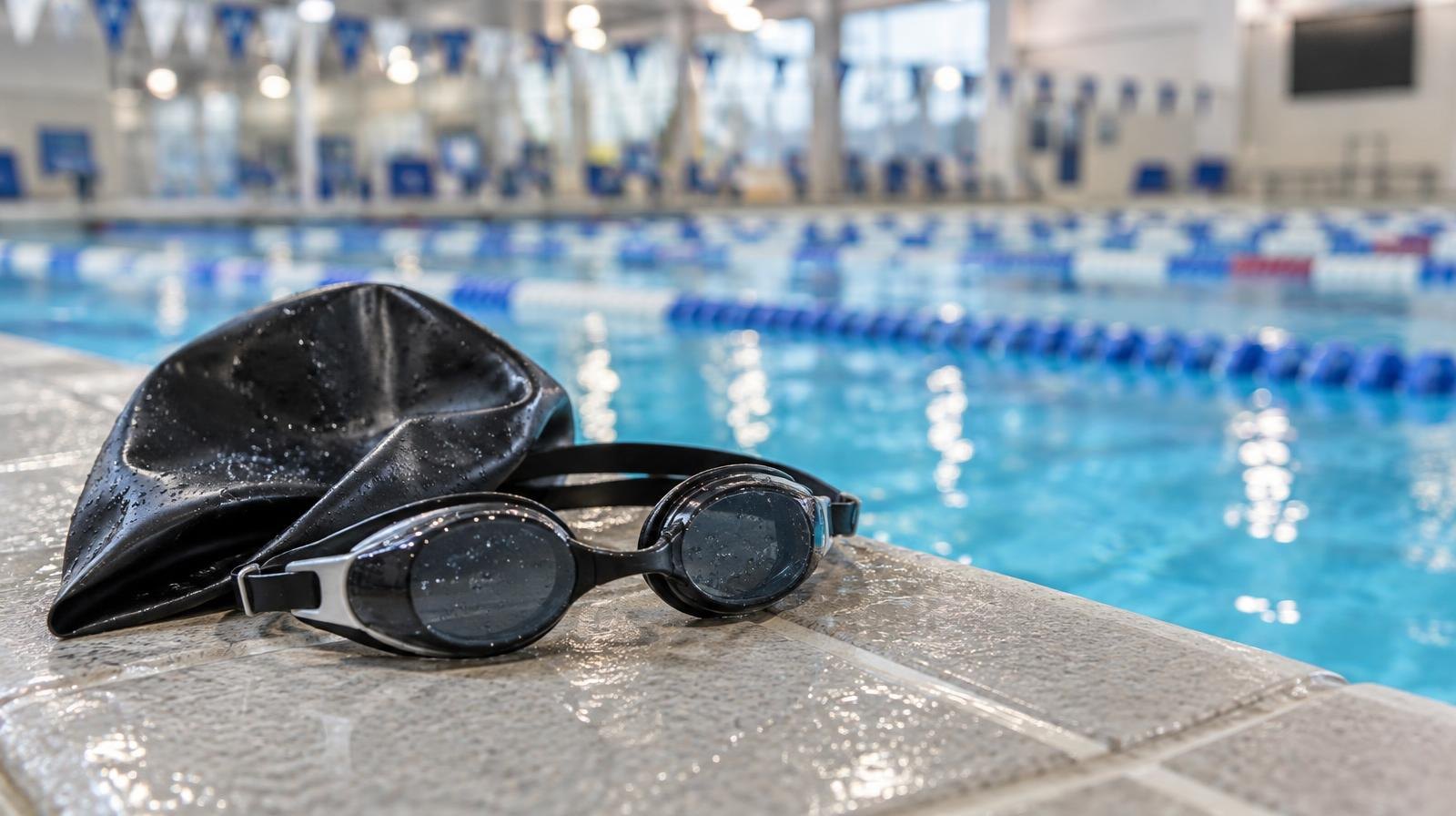Swim goggles and a cap resting on the edge of a pool lane.