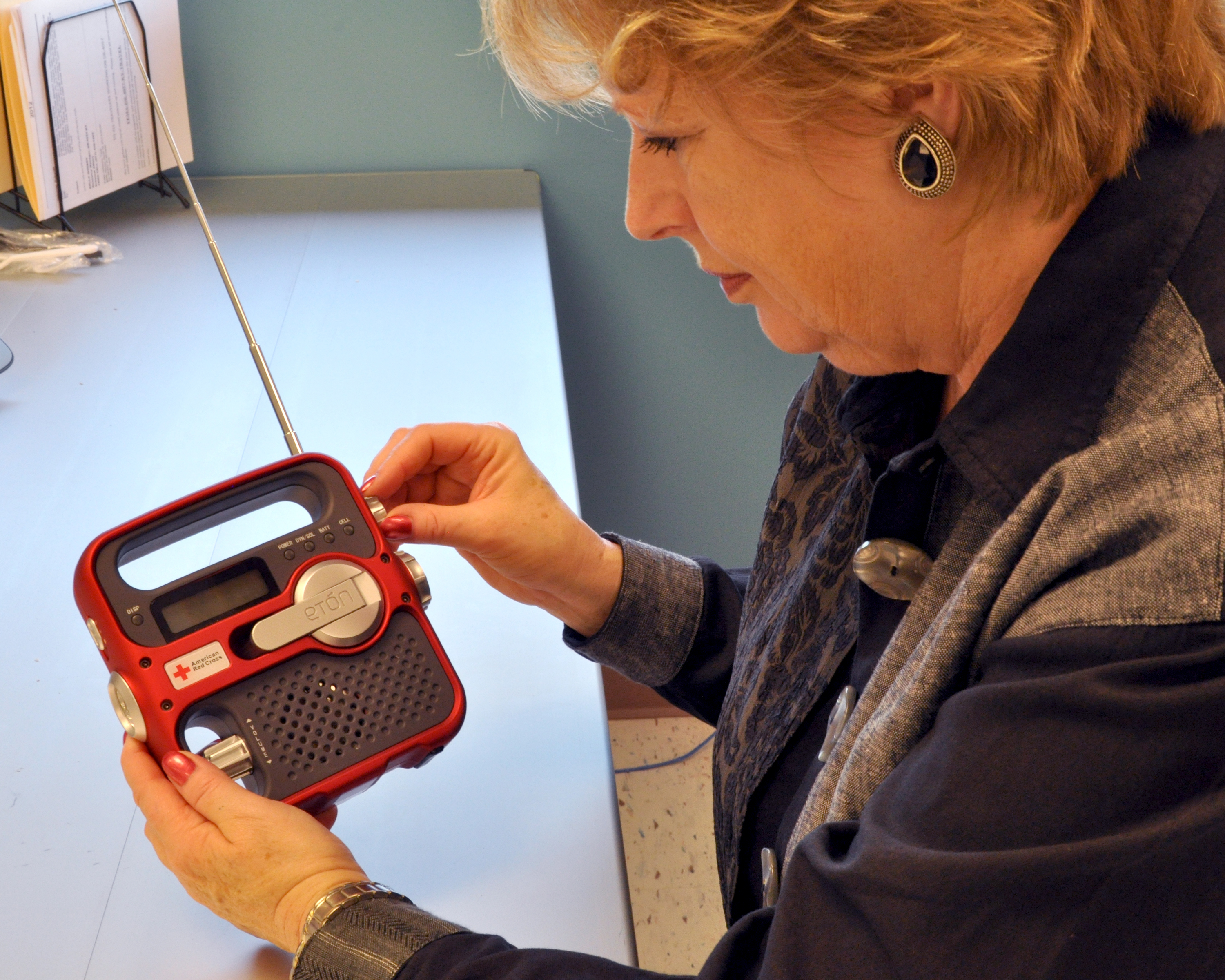 Woman holding a red hand-crank emergency weather radio with extended antenna.