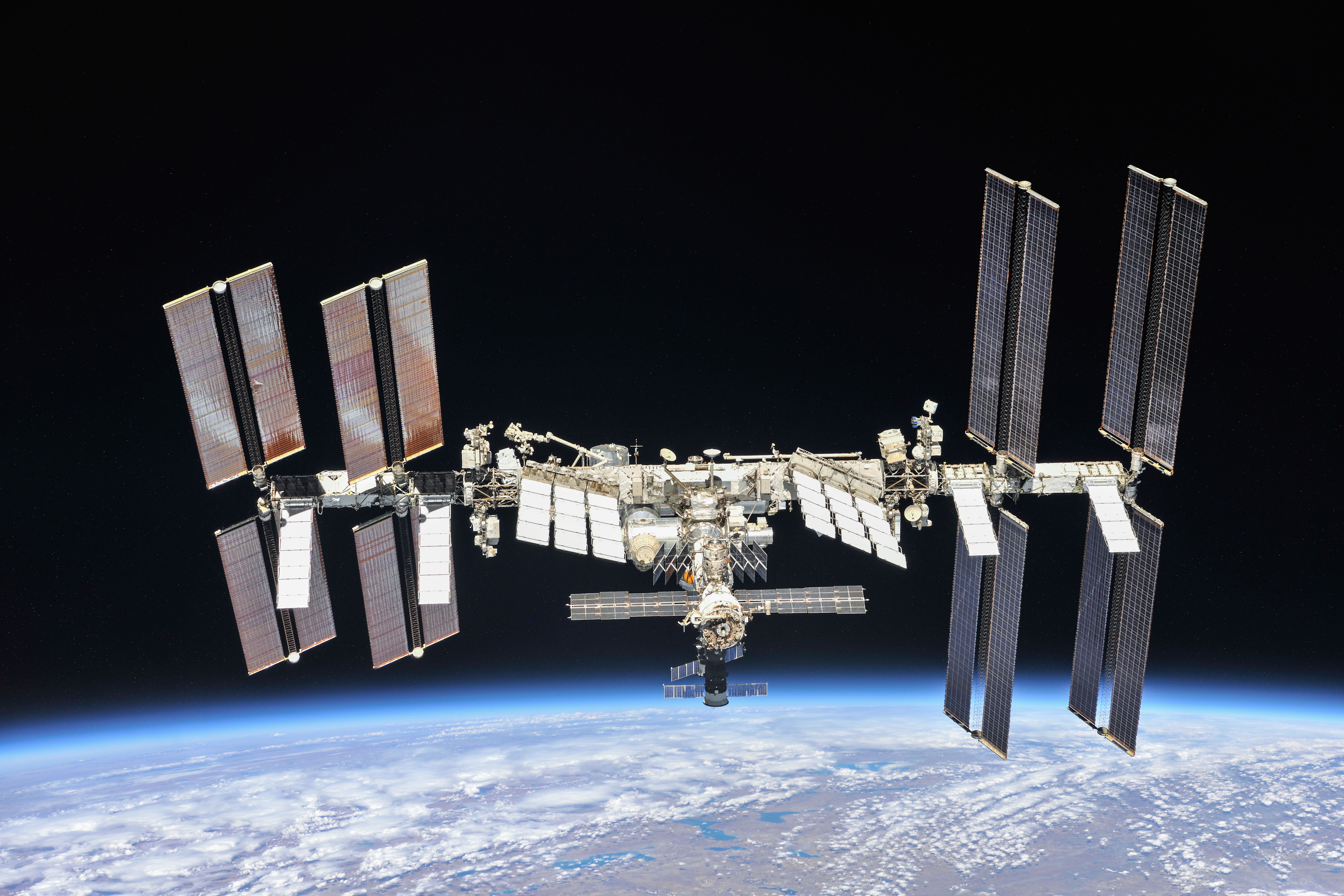 The International Space Station with large solar arrays extended, floating above Earth's atmosphere in space.