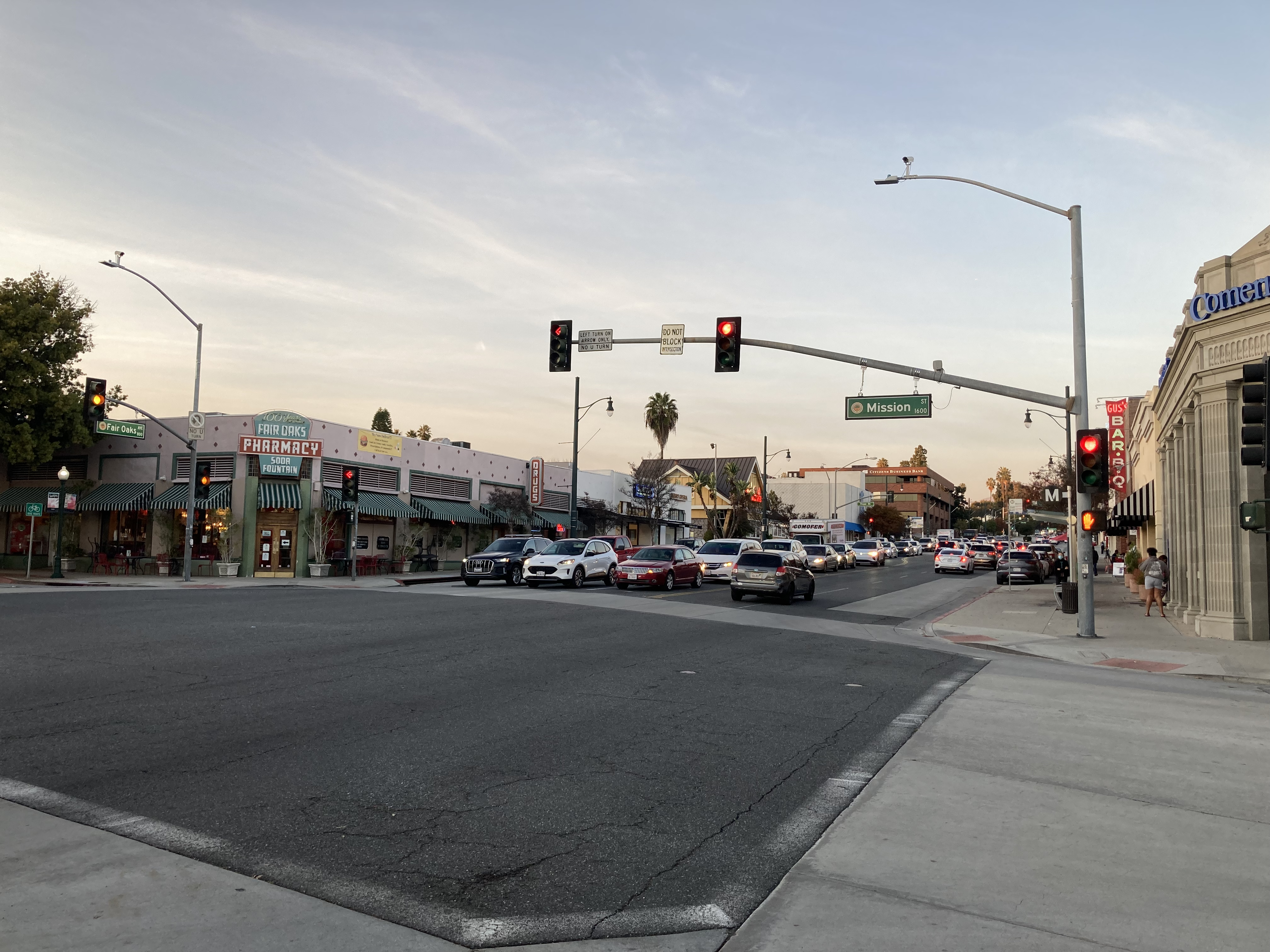 Dusk view of a commercial street intersection with traffic signals and storefronts.