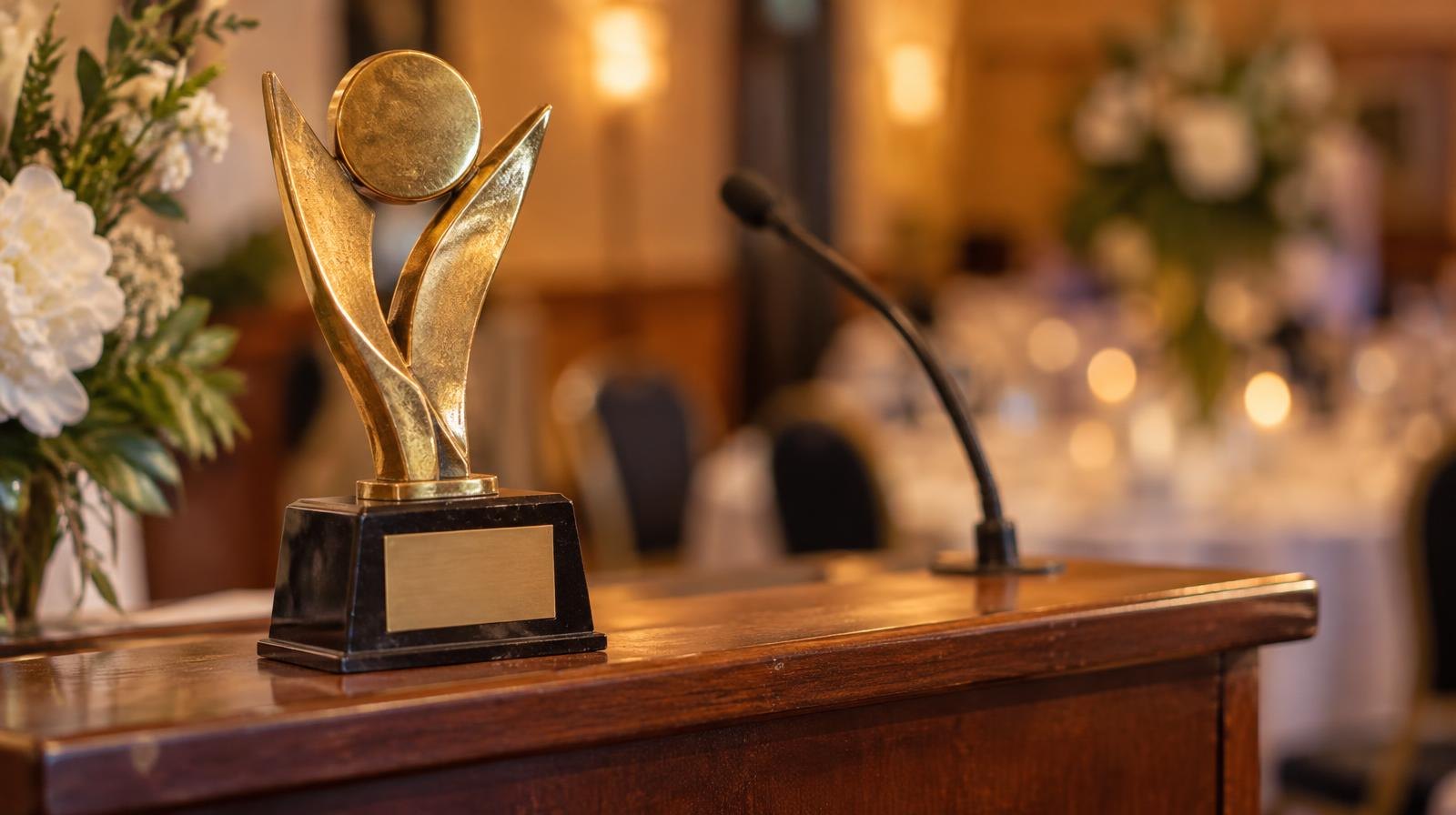 Gold award trophy on a wooden podium under warm indoor lighting.
