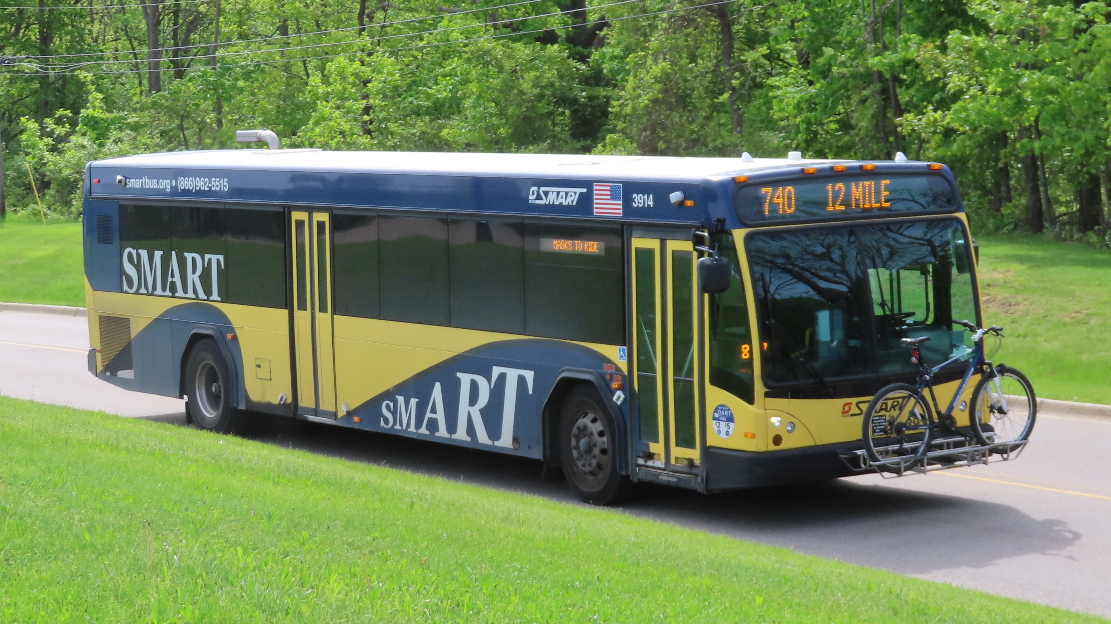 A SMART transit bus in navy blue and gold livery traveling on a tree-lined road.