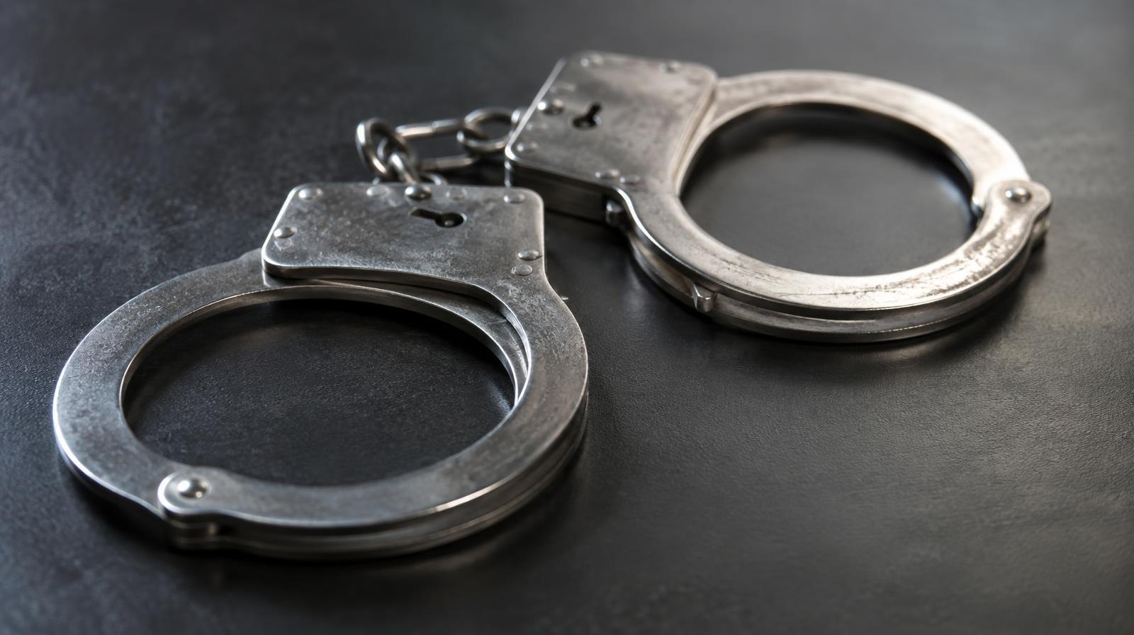 A pair of silver metal handcuffs resting on a dark surface.