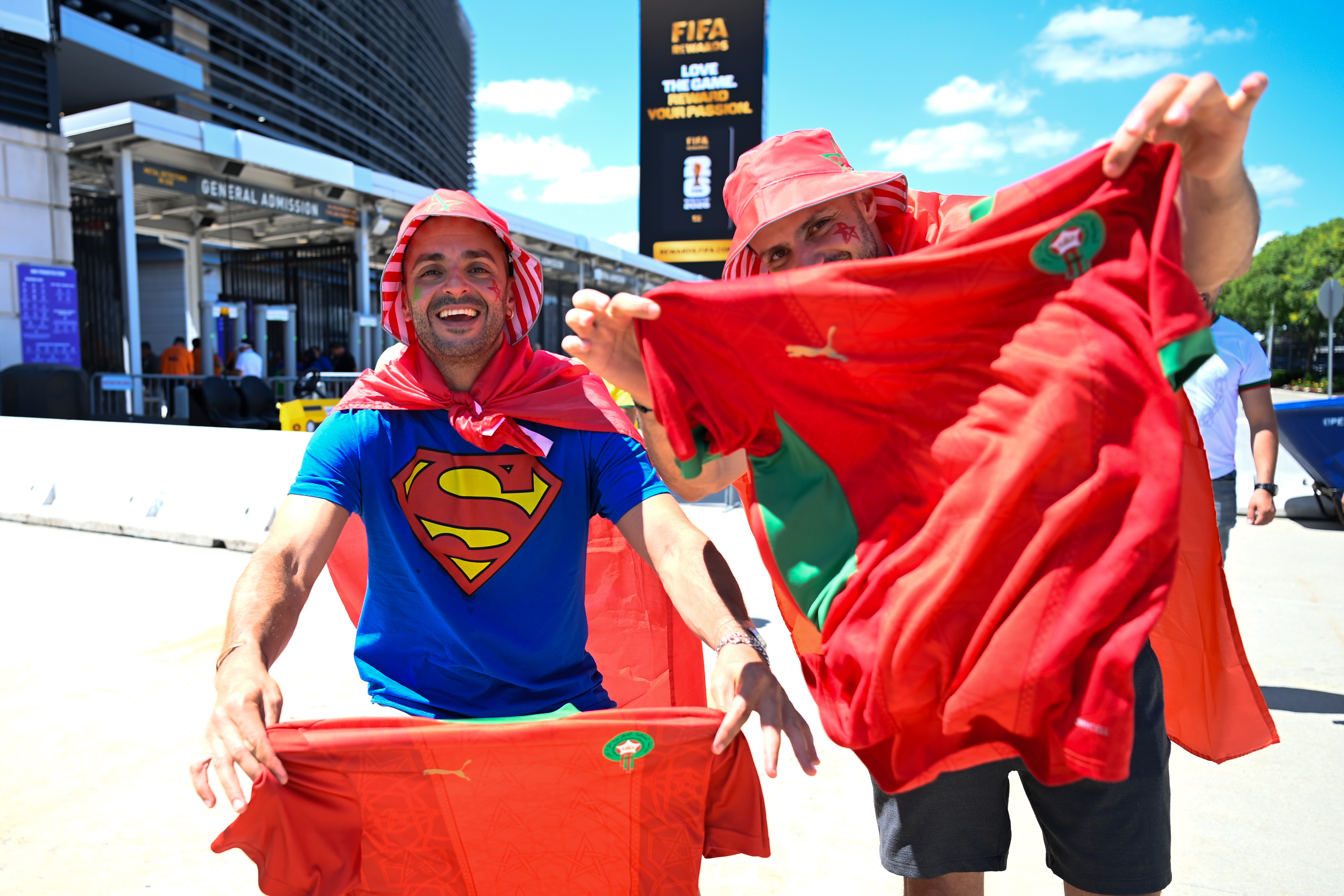 Two enthusiastic soccer fans posing with a Moroccan flag outside MetLife Stadium.