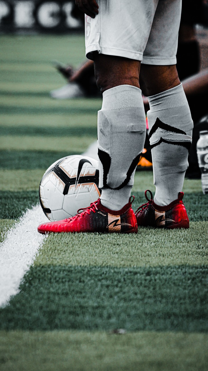A soccer player wearing gray socks and red cleats stands beside a ball near a white field line.