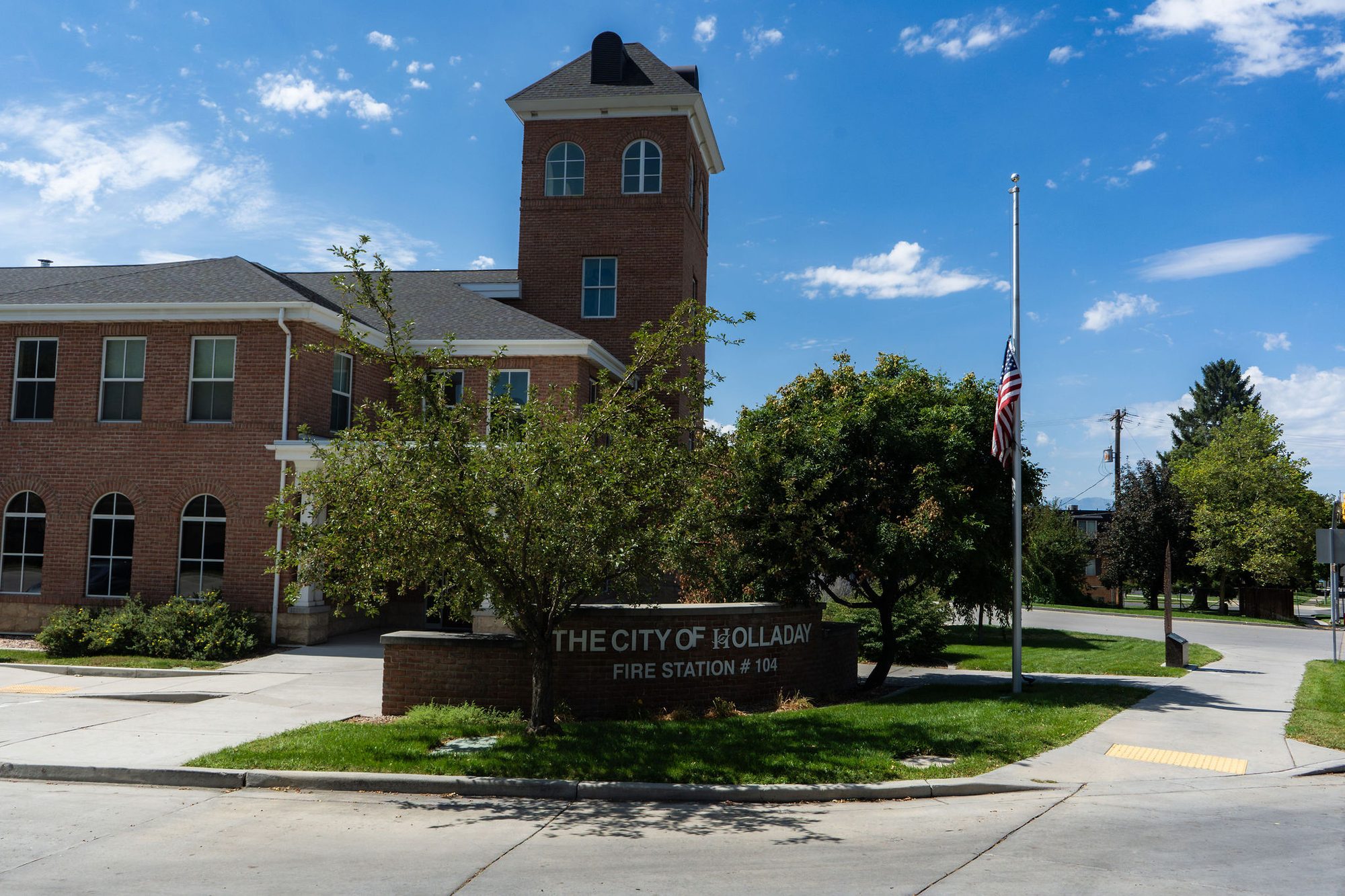 Brick fire station building with hose tower and half-staff American flag out front.