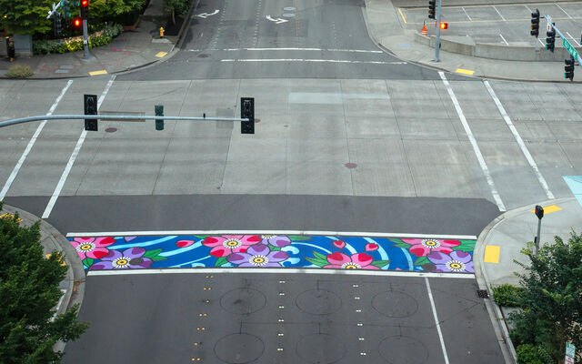 Aerial view of a brightly painted crosswalk with pink, purple, and blue floral patterns at a city intersection.
