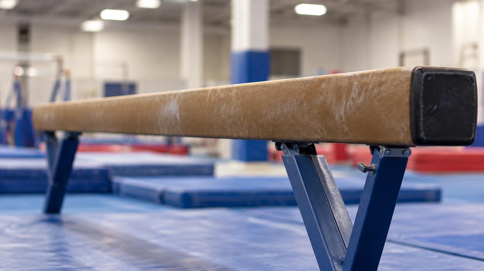 A gymnastics balance beam apparatus viewed from the side in an empty gym.