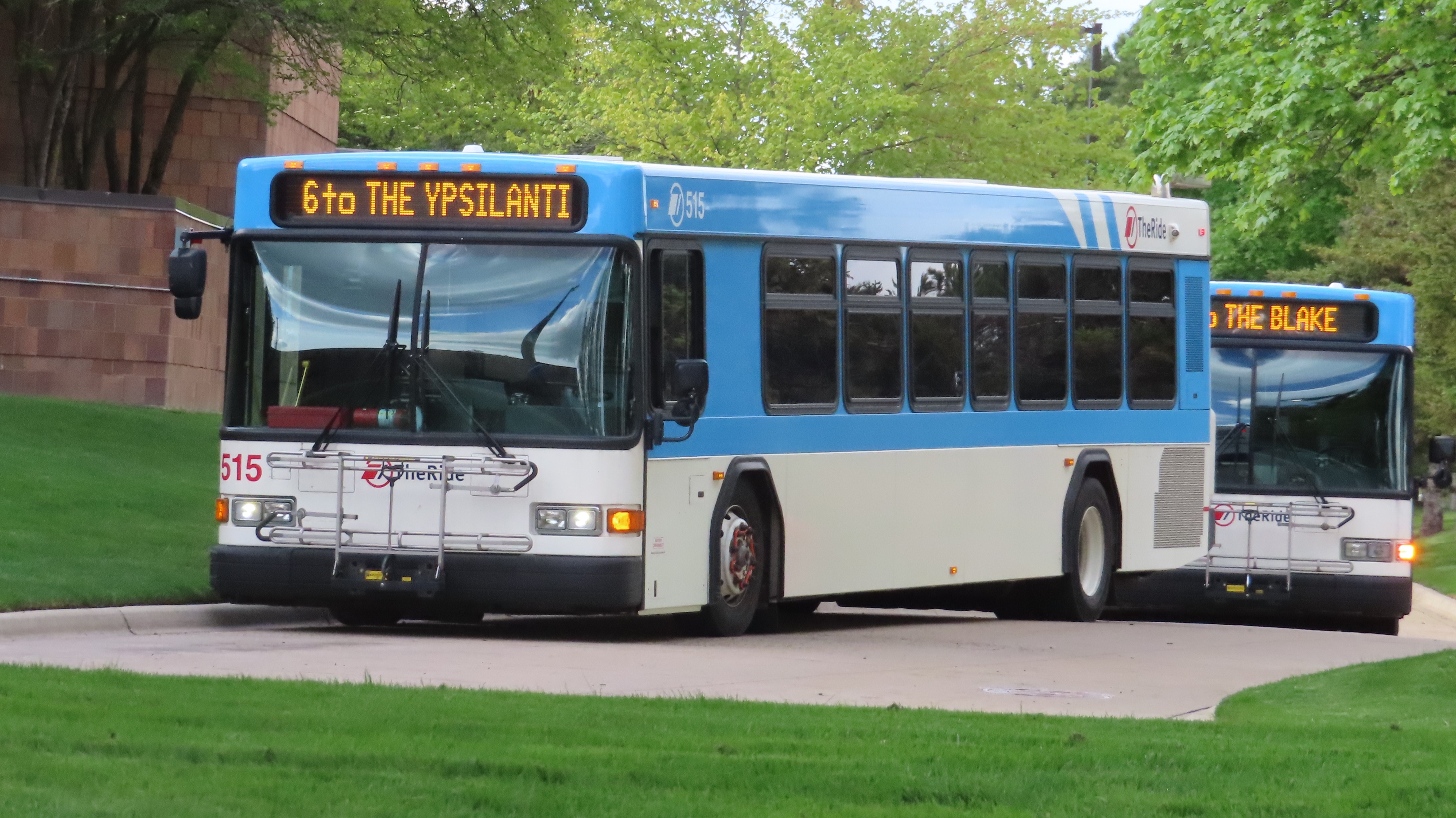 Two blue and white TheRide buses traveling on a road.