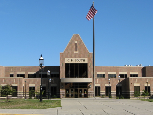Brick school building exterior with flagpole and paved entrance plaza.