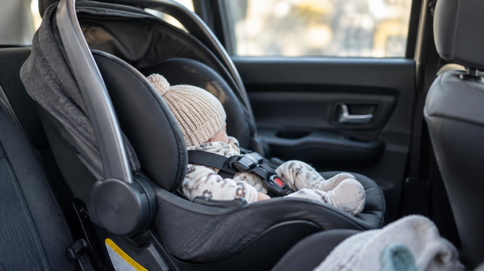 A rear-facing infant car seat buckled securely in a vehicle back seat.