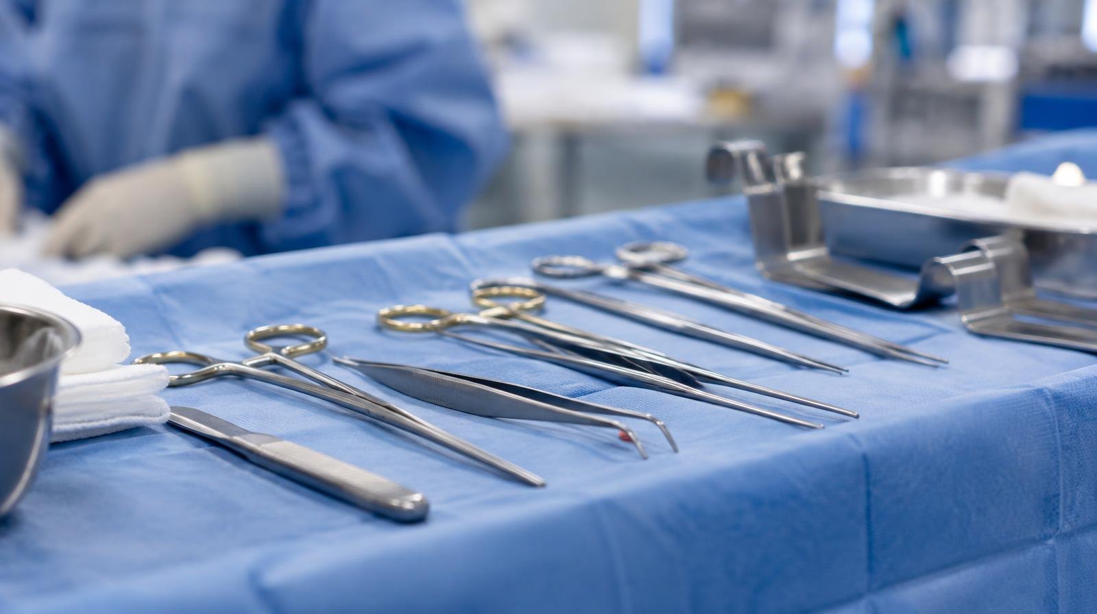 Stainless steel forceps, retractors, and scissors on a blue surgical drape.
