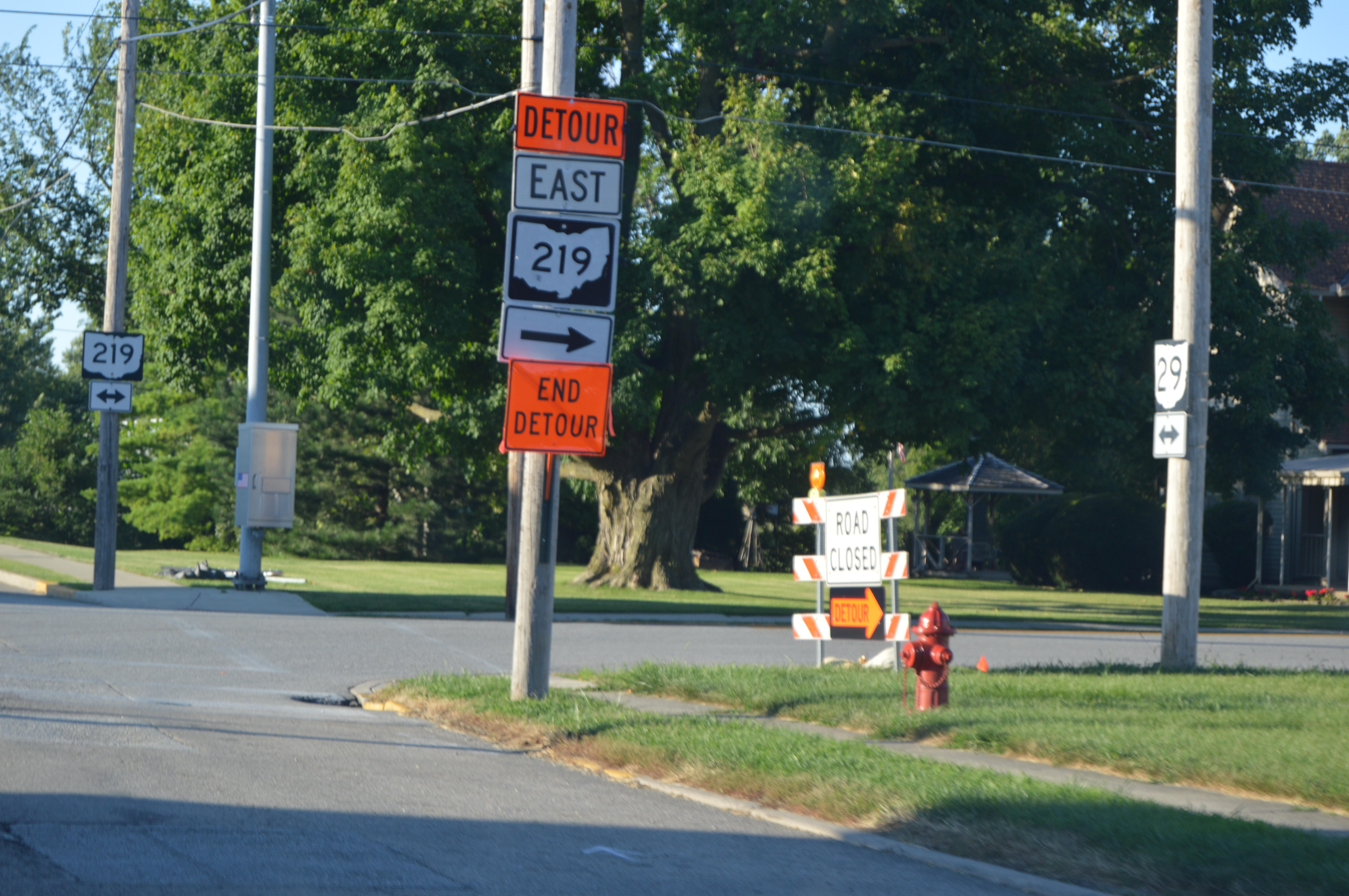 Orange detour signs on a roadside pole near a construction barrier.